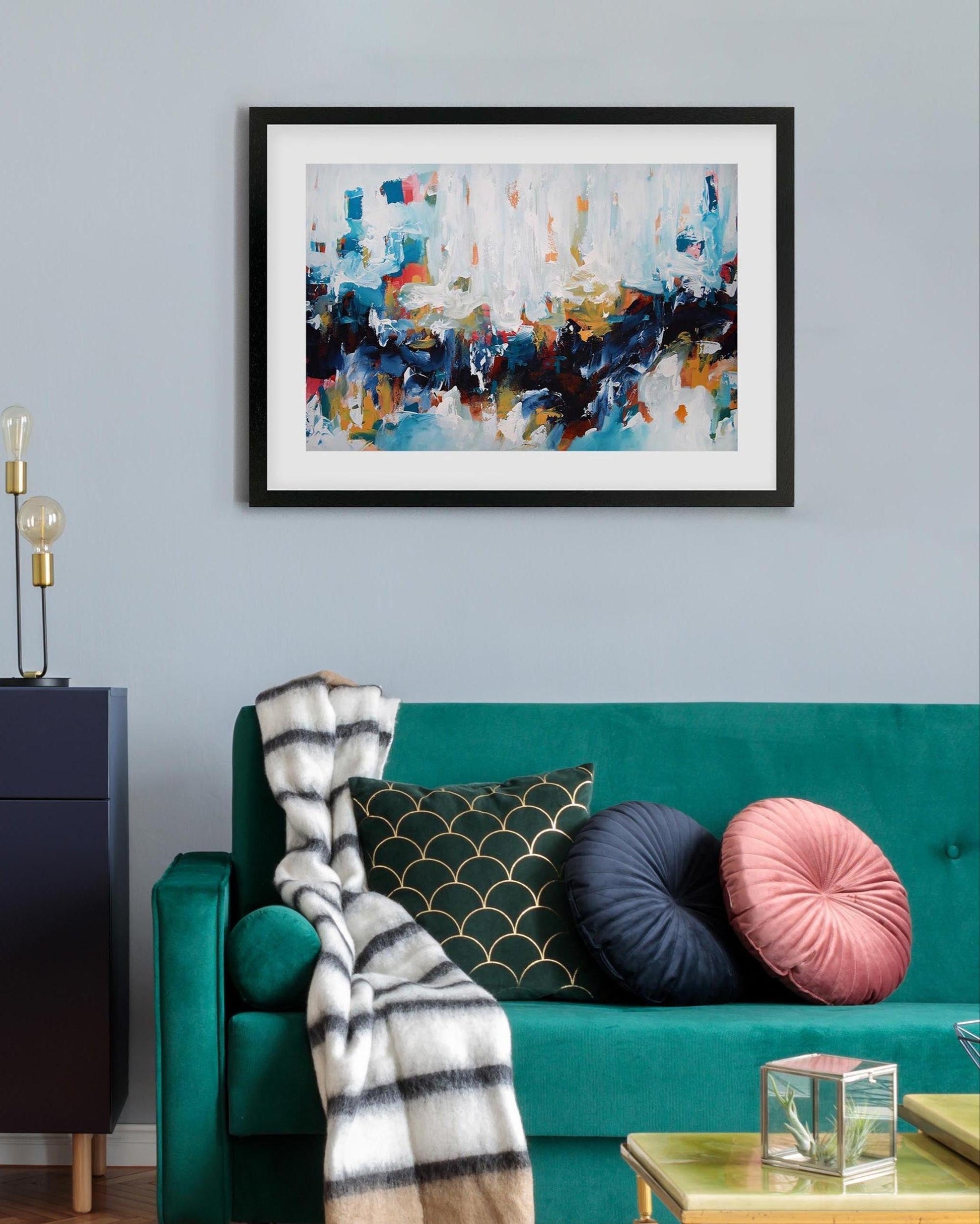 Framed abstract art above a teal sofa with decorative pillows and a blanket.