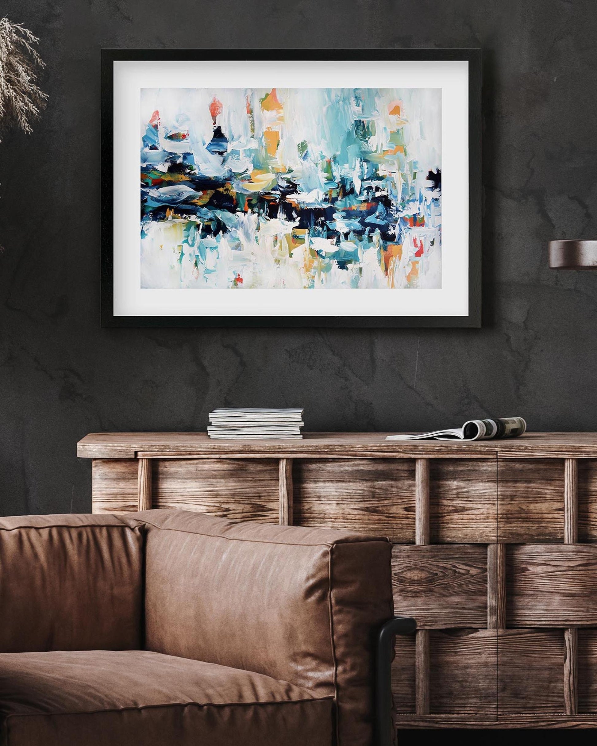 Framed abstract painting on a dark wall above a brown sofa and wooden console table.