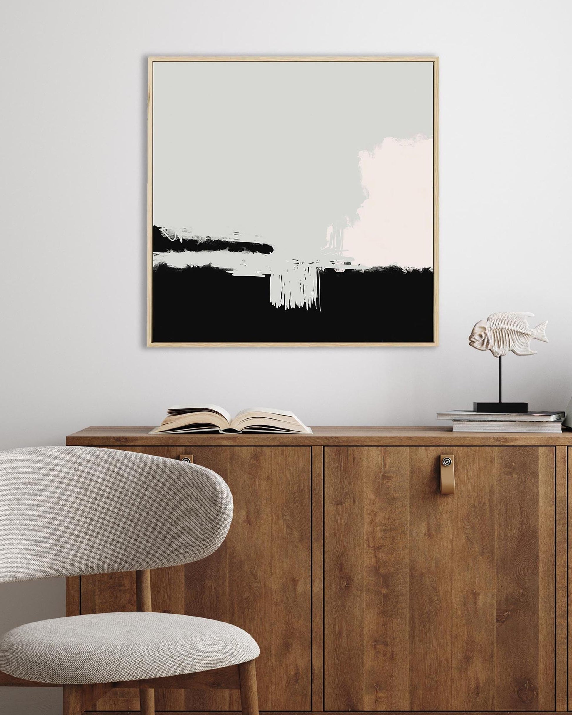 Abstract art piece on a wall above a wooden cabinet with a chair and books.