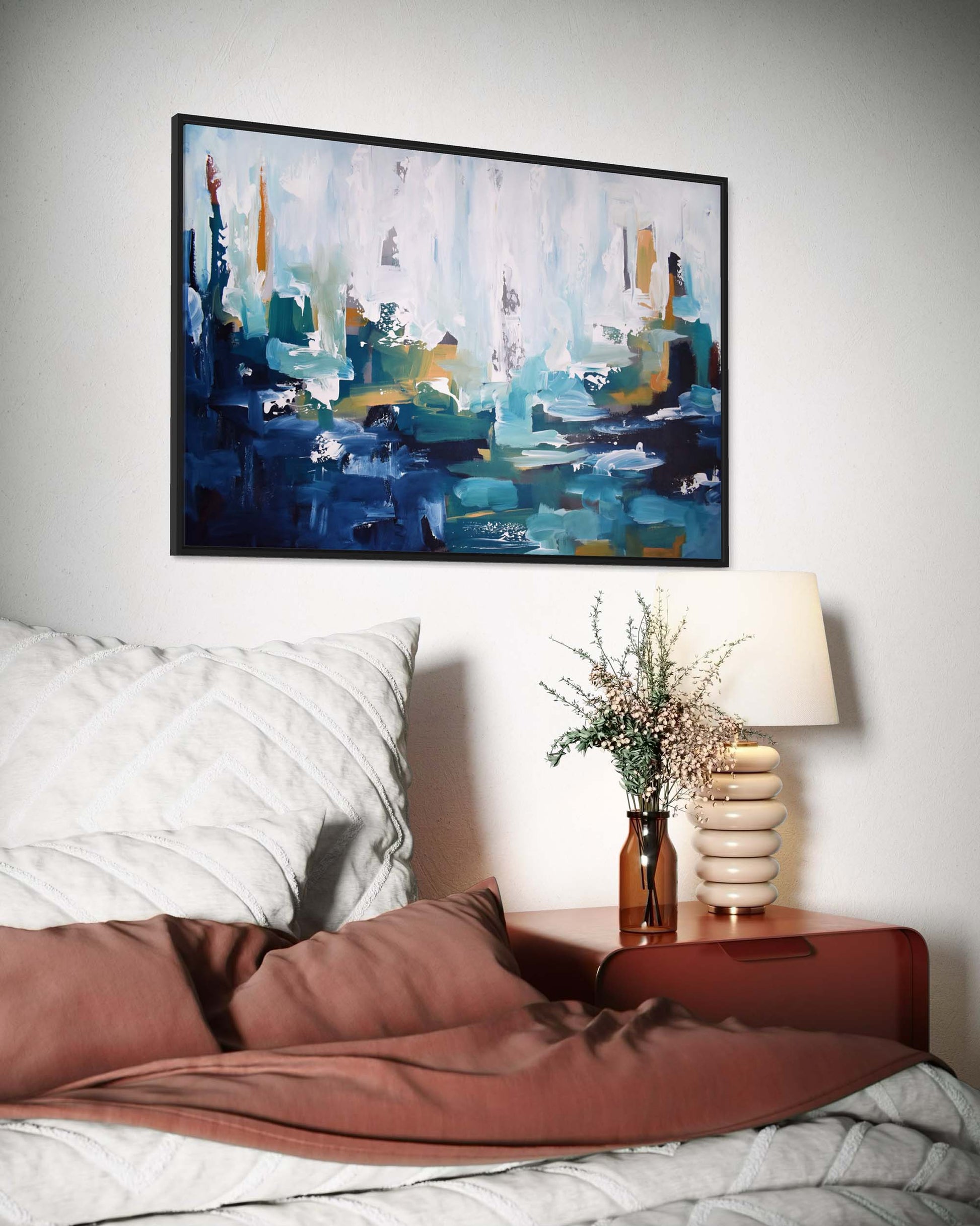 Abstract painting above a bed with a side table and lamp in a bedroom setting