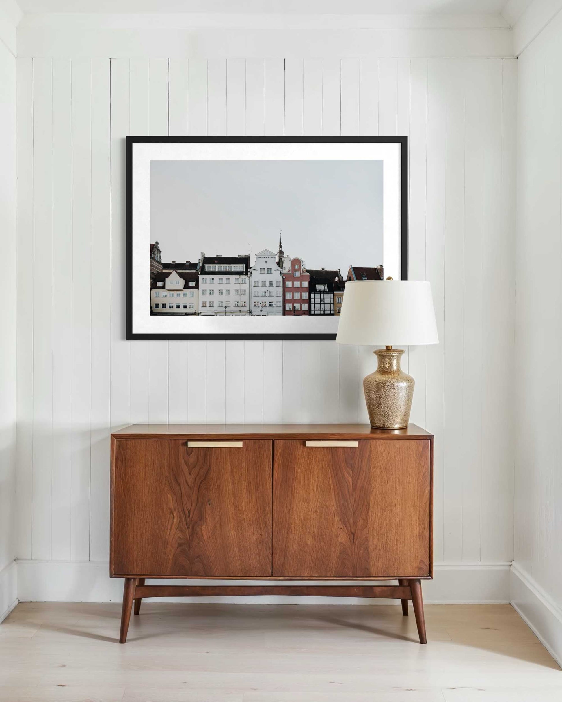 Wooden sideboard with a lamp and framed picture on a white wall