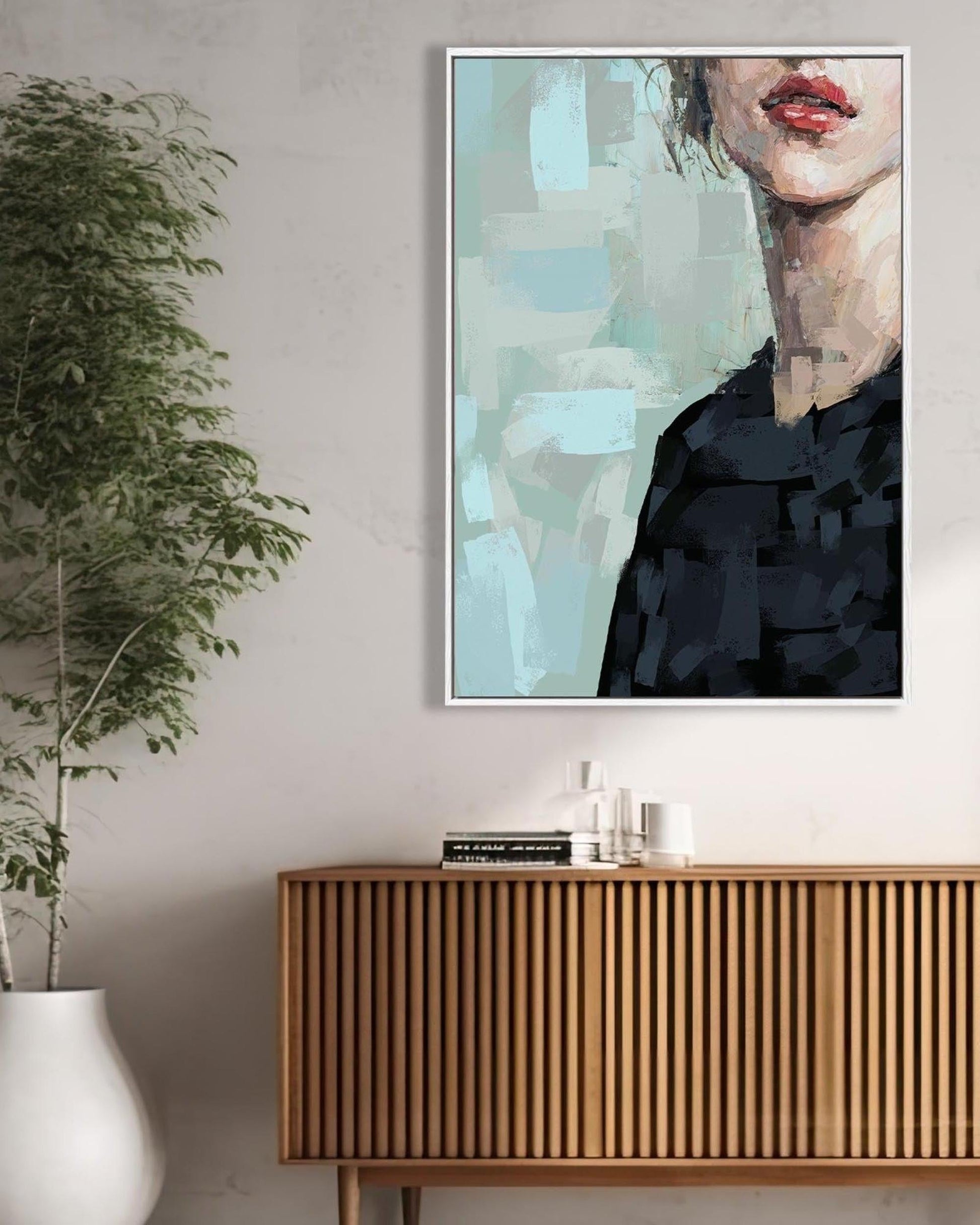 Framed abstract art on a wall above a wooden cabinet with a plant to the left.