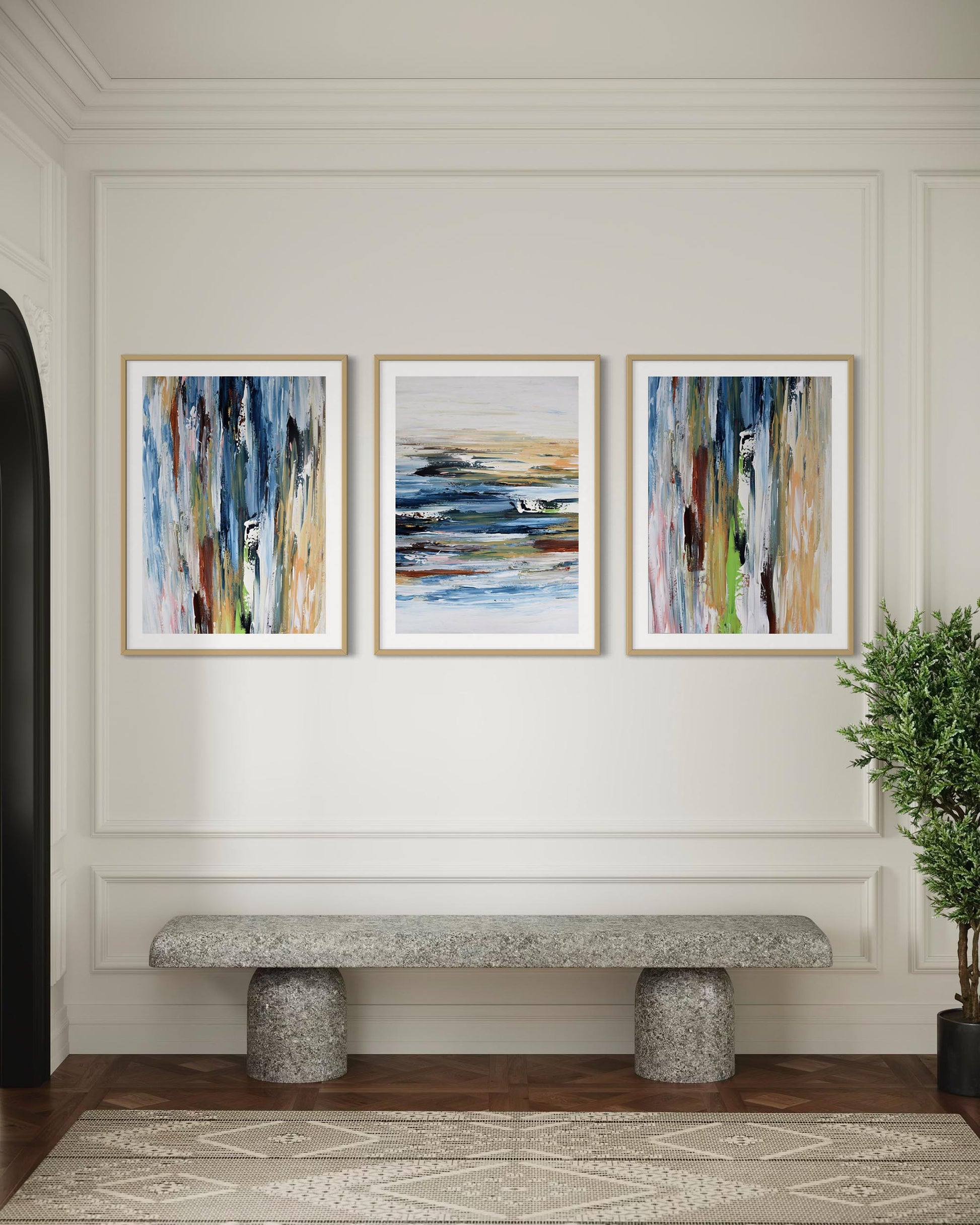 Three abstract paintings on a wall above a stone bench in a room with a plant.