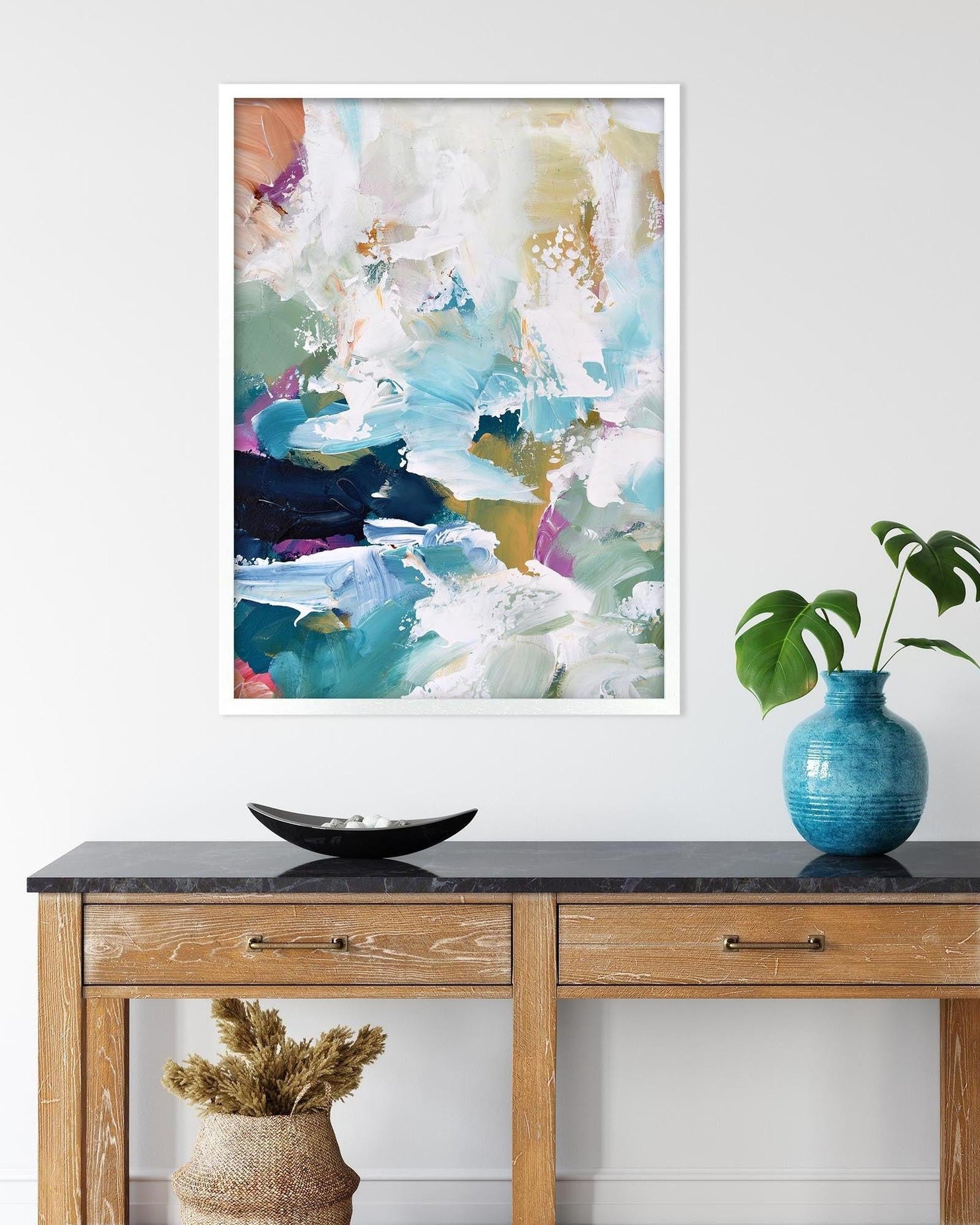Abstract art print on a wall above a wooden console table with decorative items.