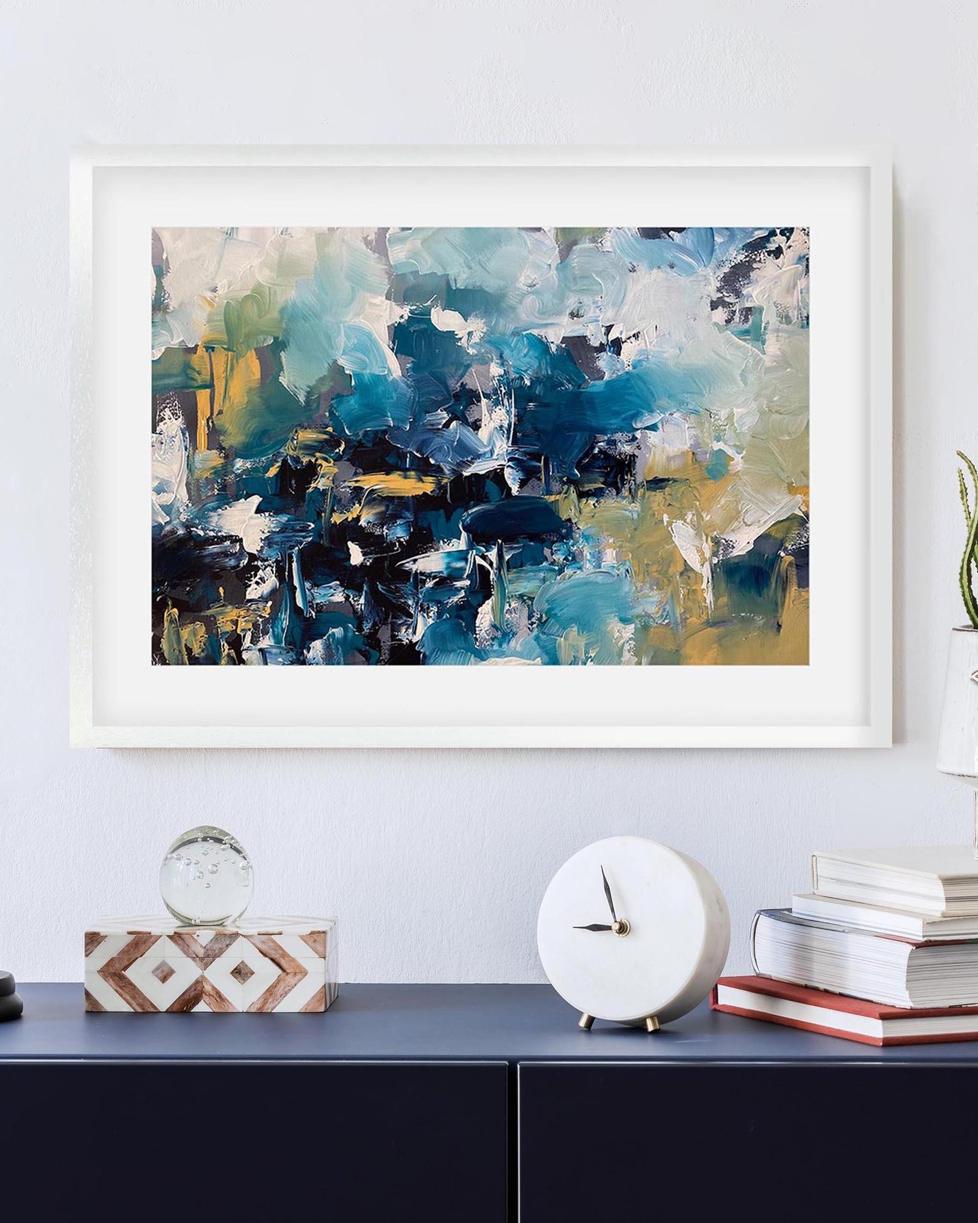 Framed abstract art piece on a wall above a shelf with decorative items.