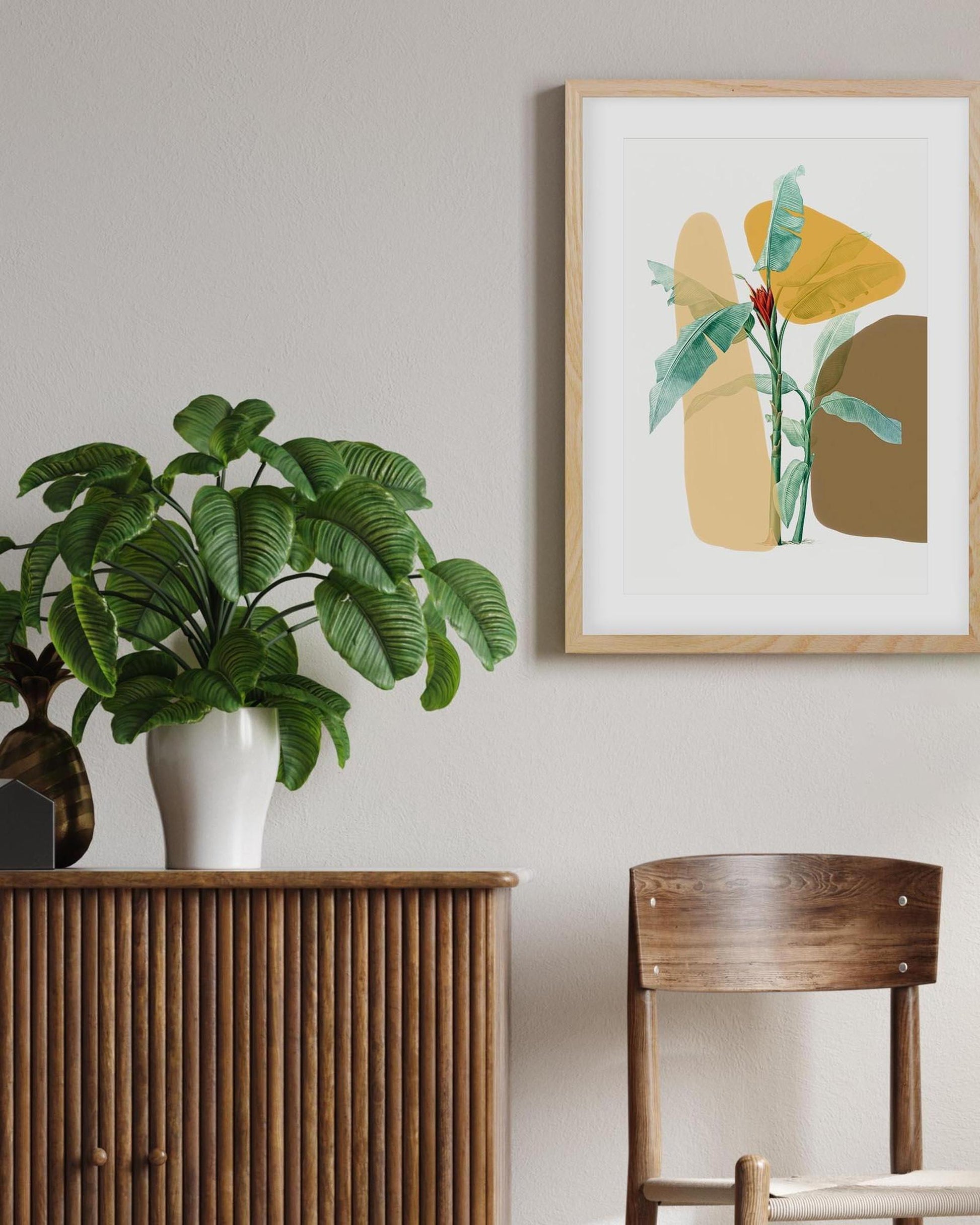 Framed abstract art on a wall with a plant and wooden furniture in the foreground.