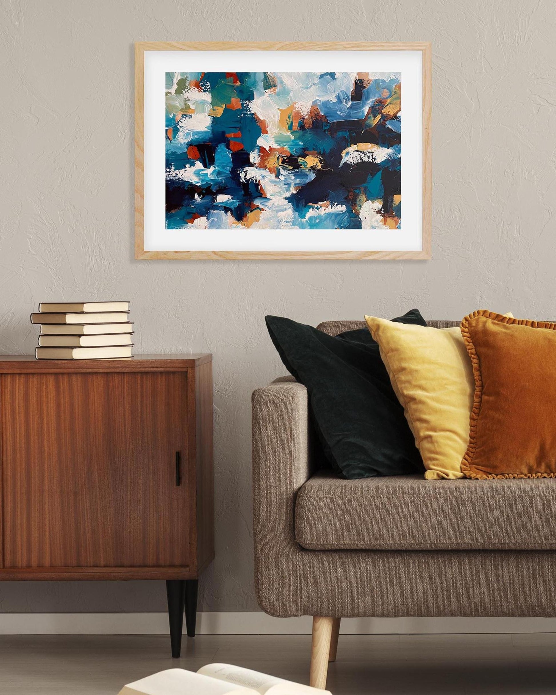 Abstract art print on a wall above a sofa with colorful pillows