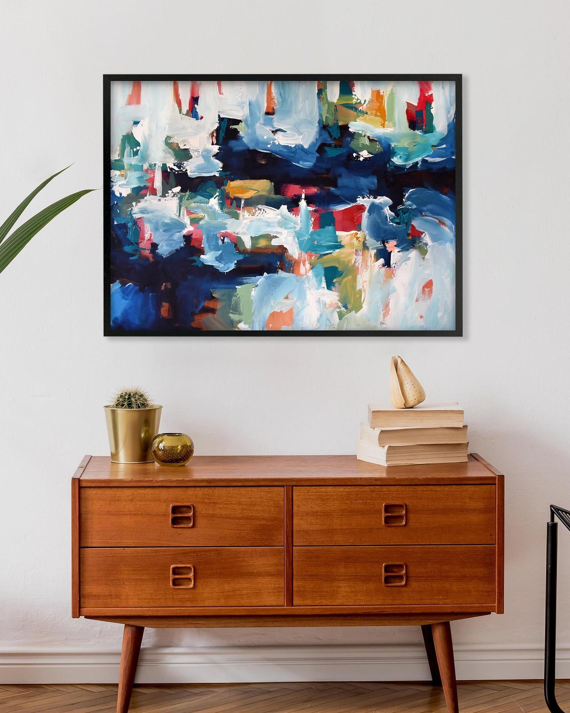 Abstract painting above a wooden dresser with decorative items.