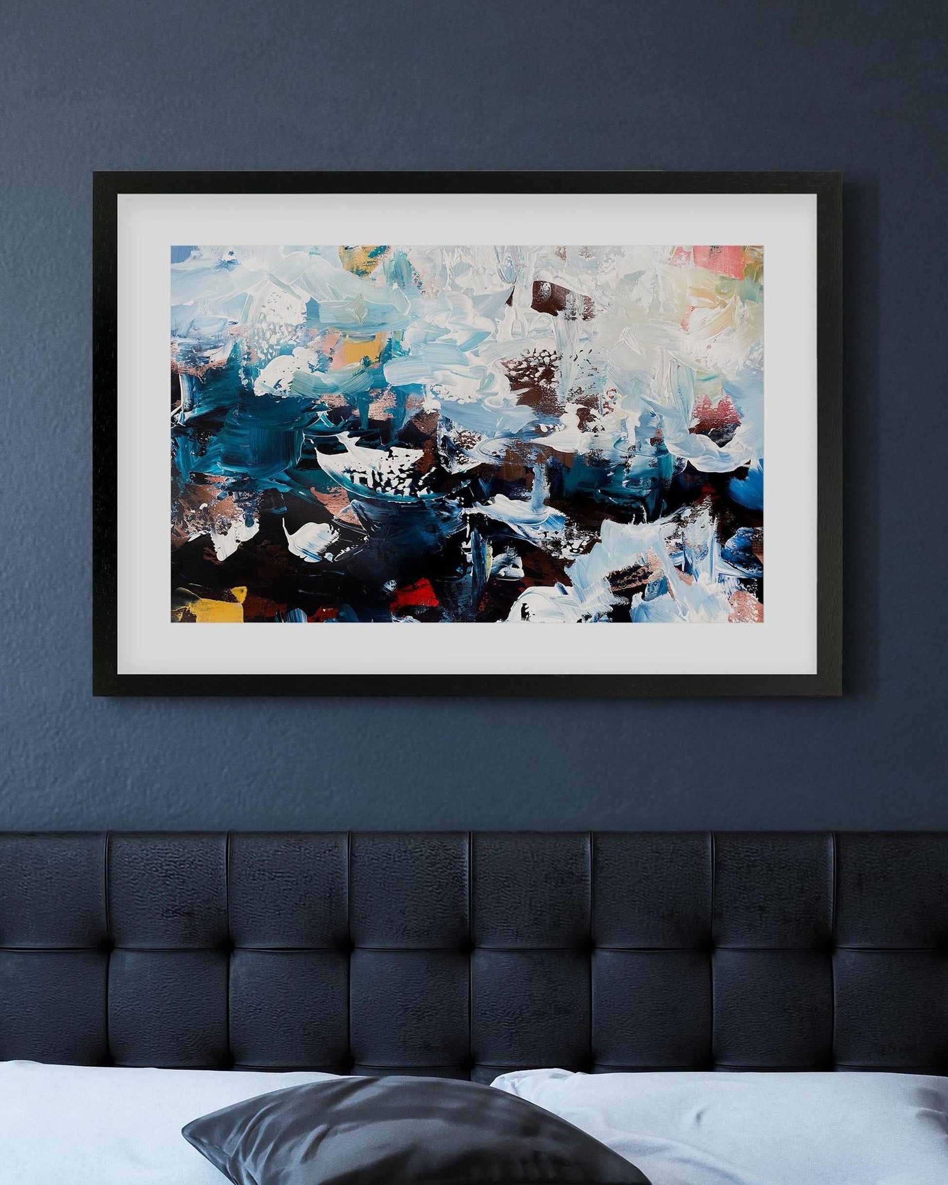 Framed abstract painting on a dark blue wall above a bed.