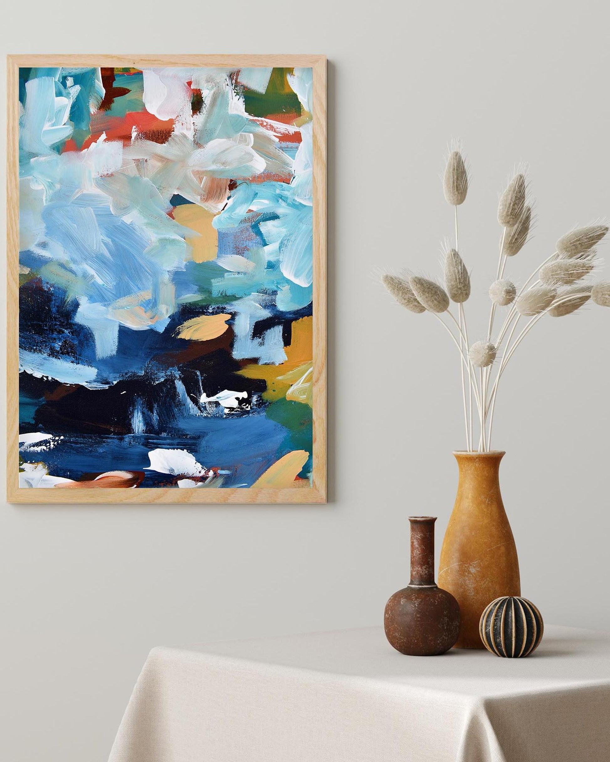 Abstract painting in a wooden frame on a wall above a table with decorative vases.
