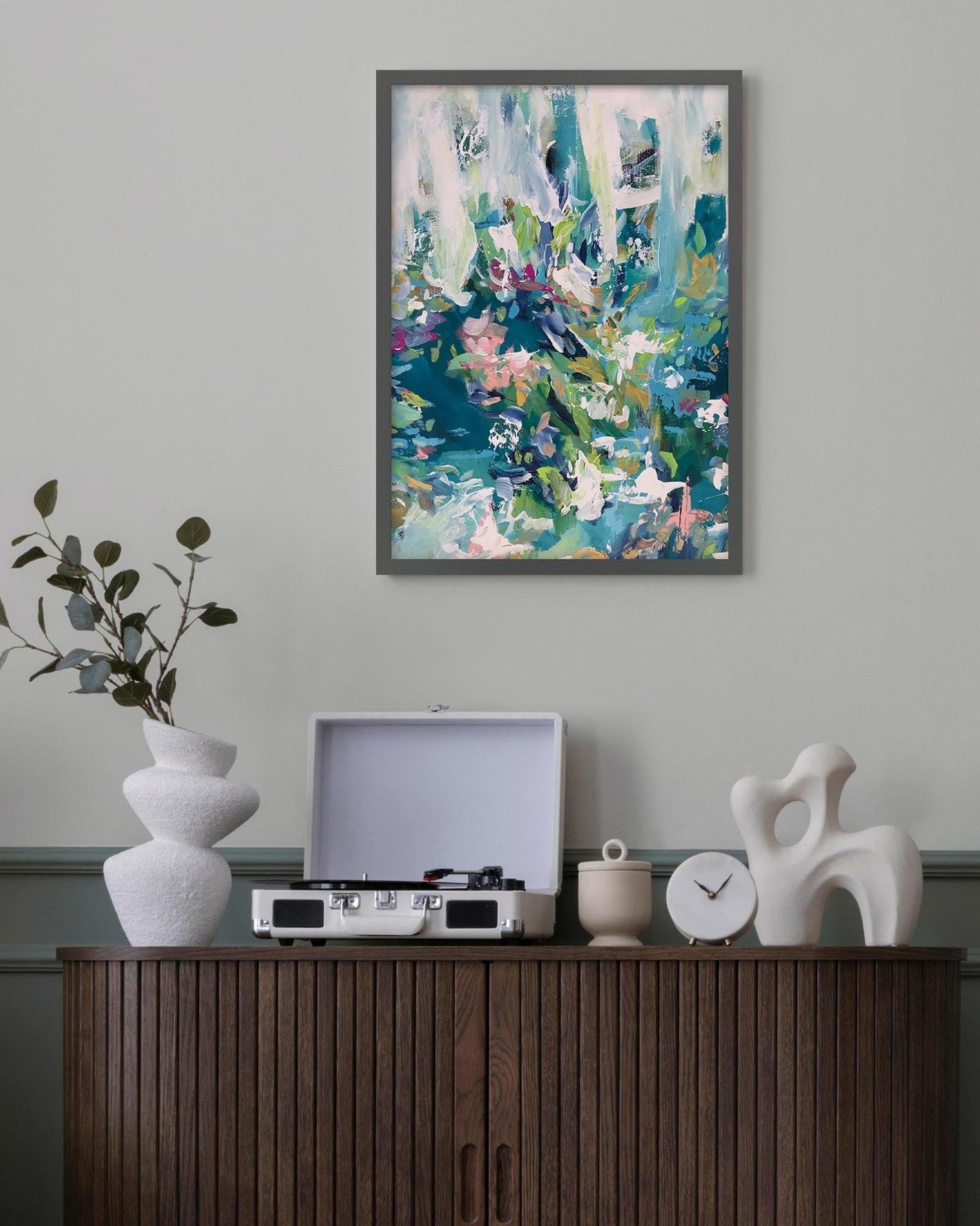 Abstract painting on a wall above a wooden cabinet with decorative items.