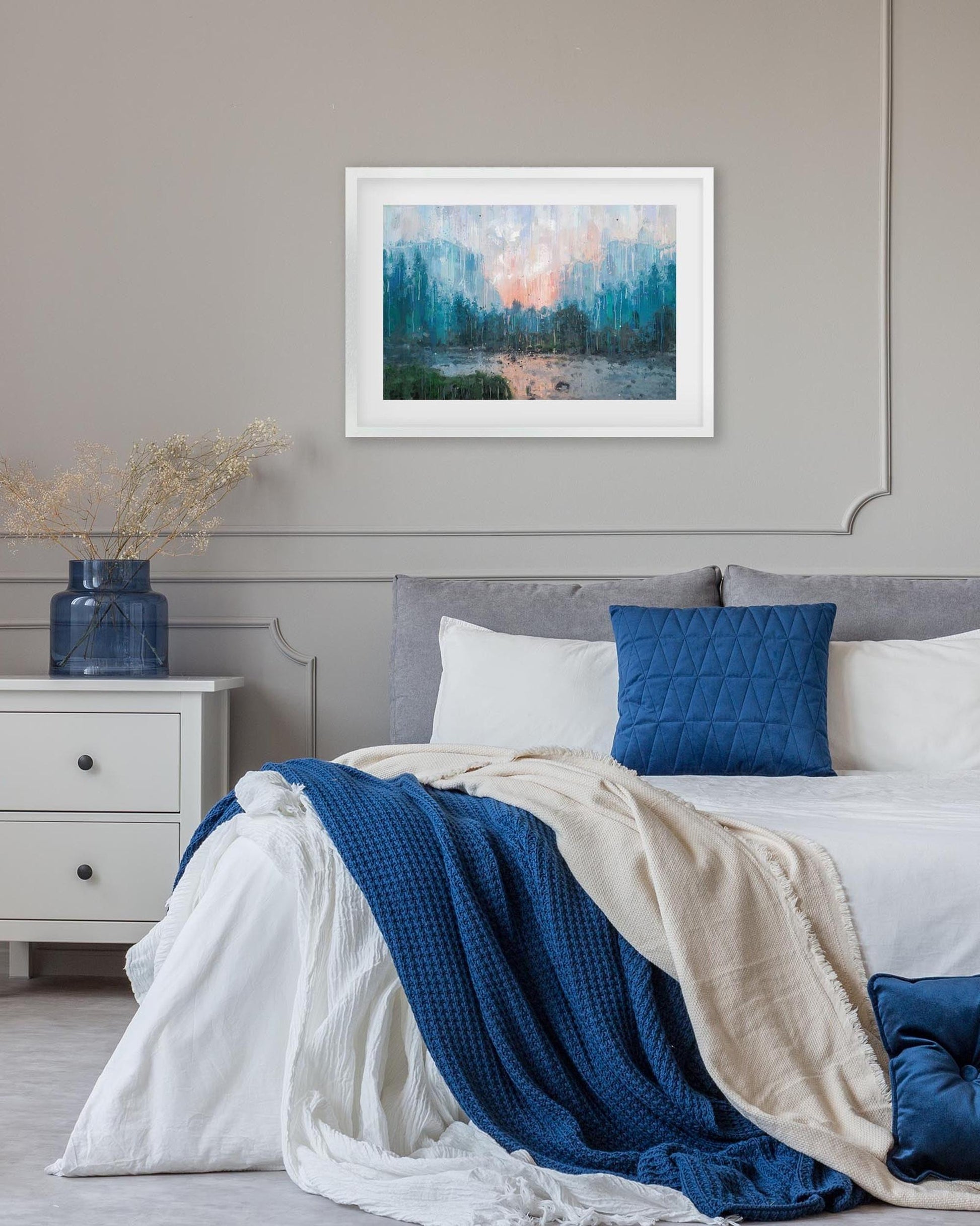 Framed abstract artwork above a bed with blue and white bedding.
