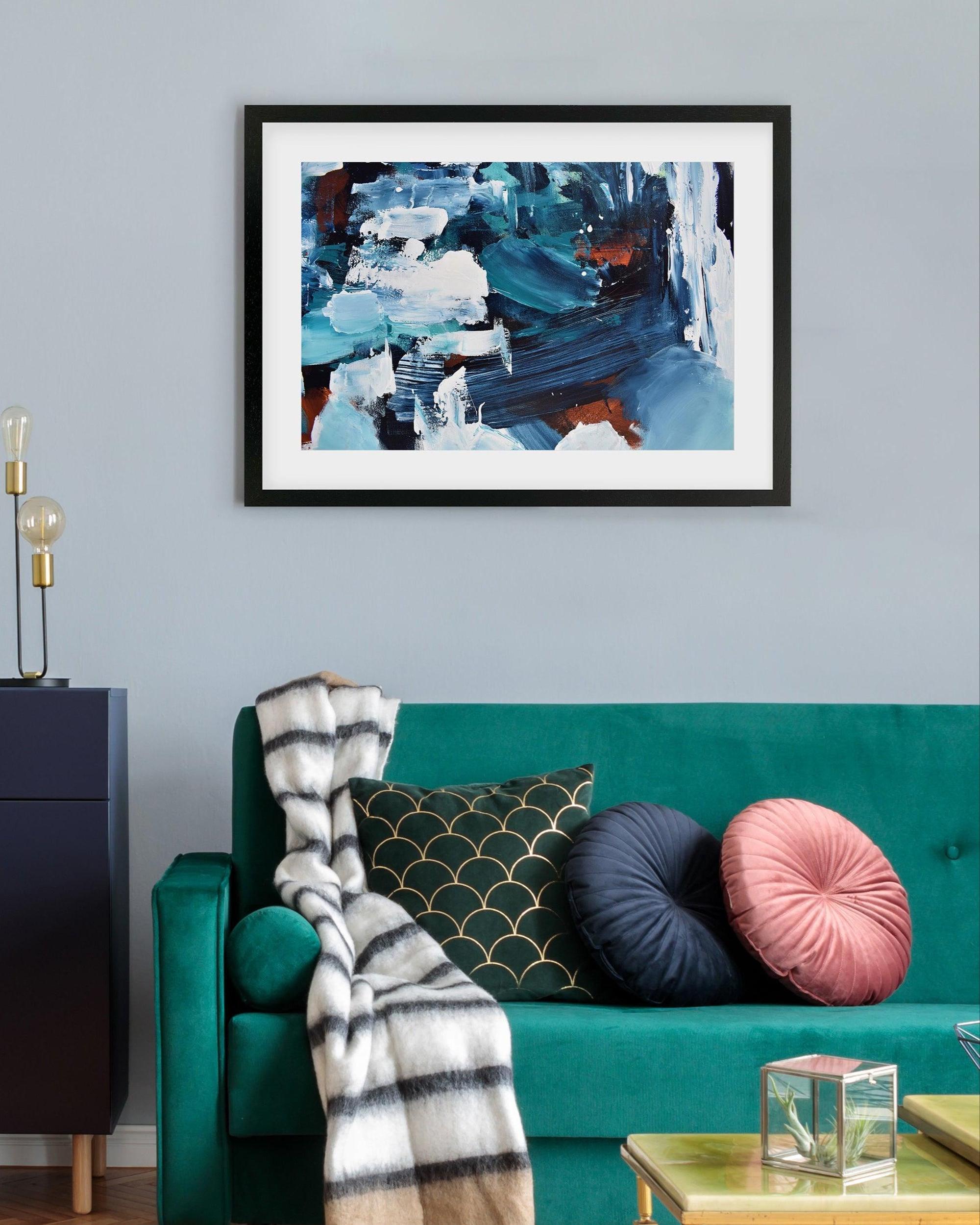 Framed abstract painting on a wall above a teal sofa with decorative pillows.