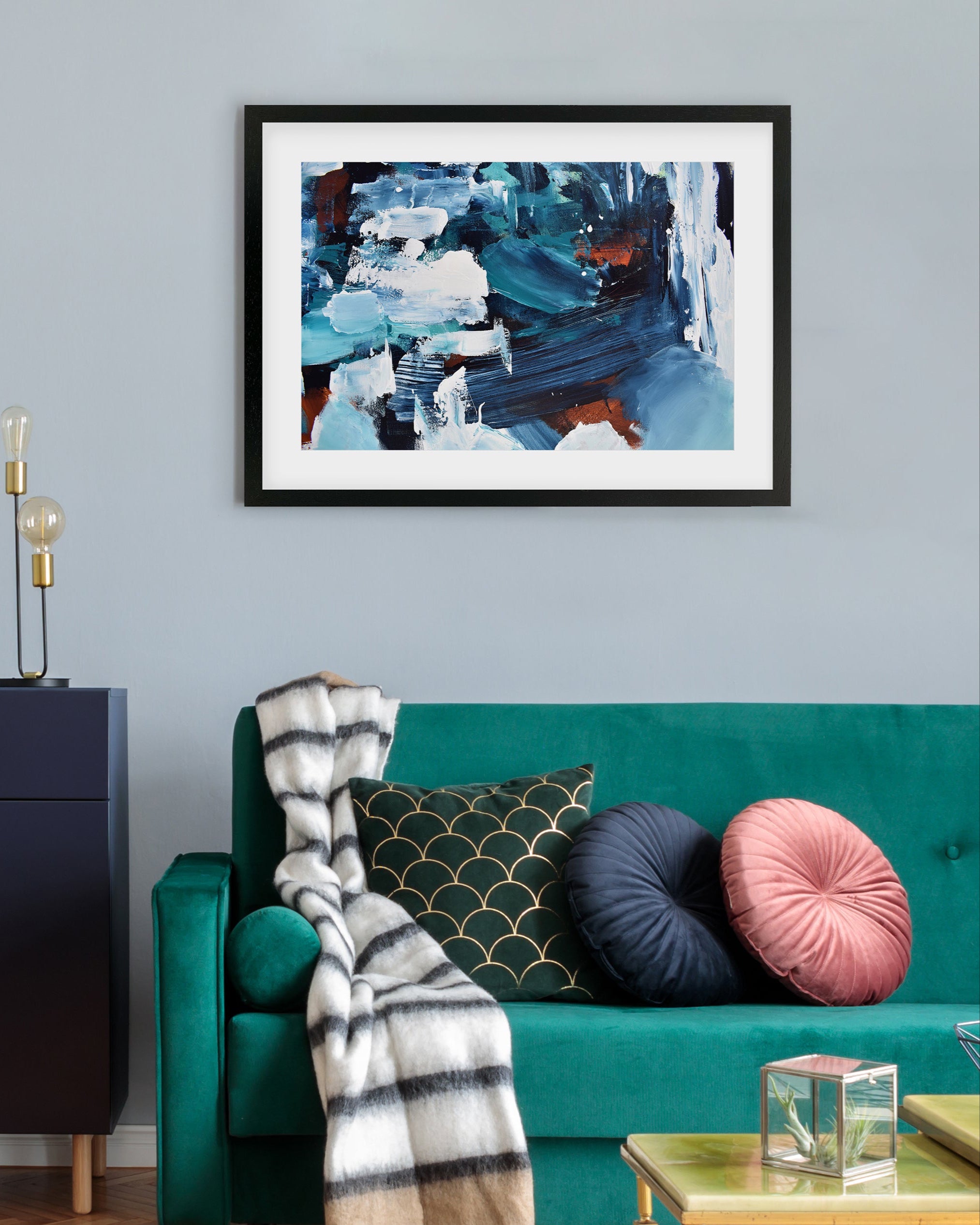 Framed abstract painting on a wall above a teal sofa with decorative pillows.