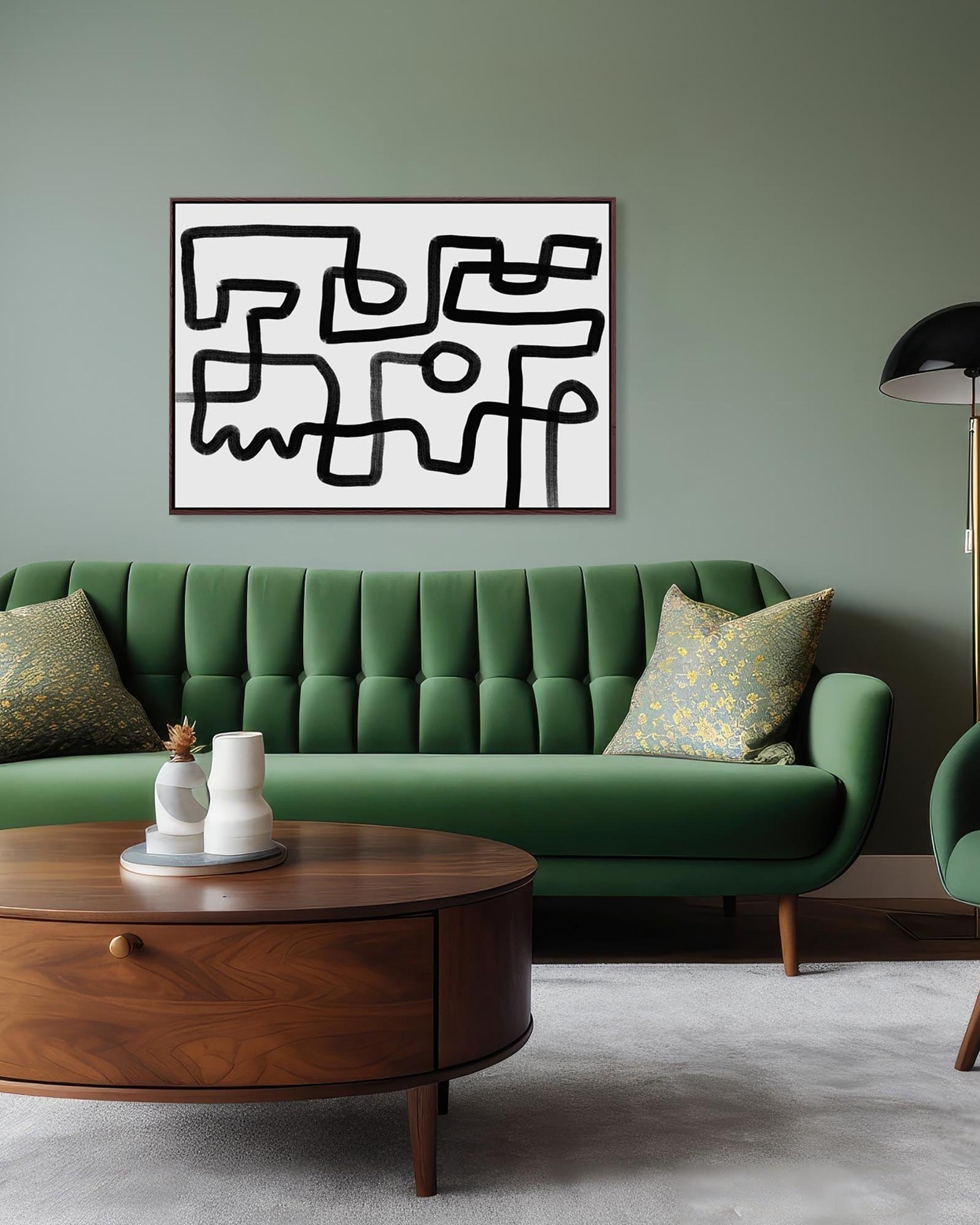 A black and white geometric maze canvas art hanging on a wall above a green sofa, with a wooden coffee table and a floor lamp in the foreground.
