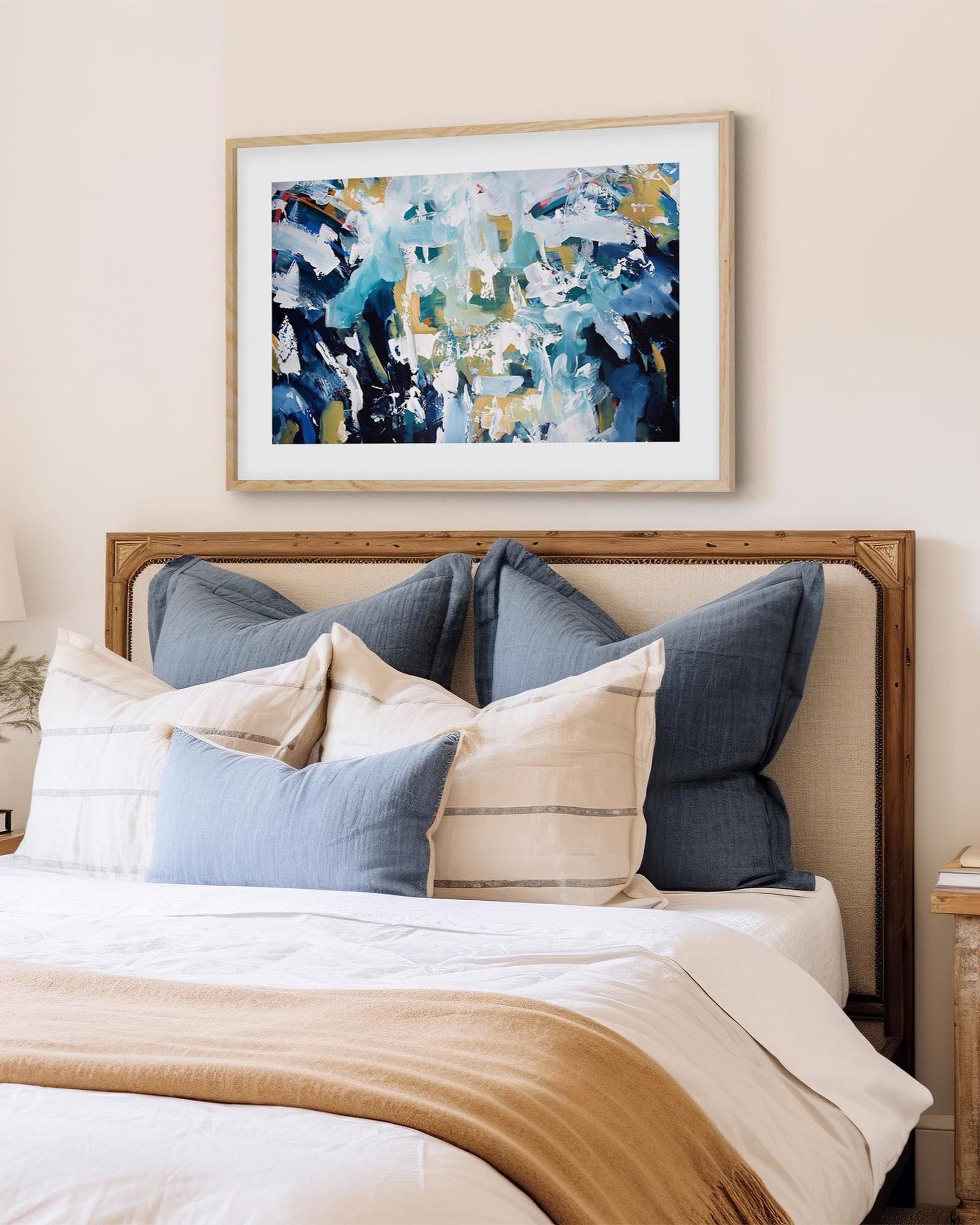 Bedroom with a bed featuring blue and beige pillows, a wooden headboard, and abstract art on the wall.
