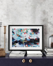 Framed abstract art piece on a shelf with decorative items against a gray wall.
