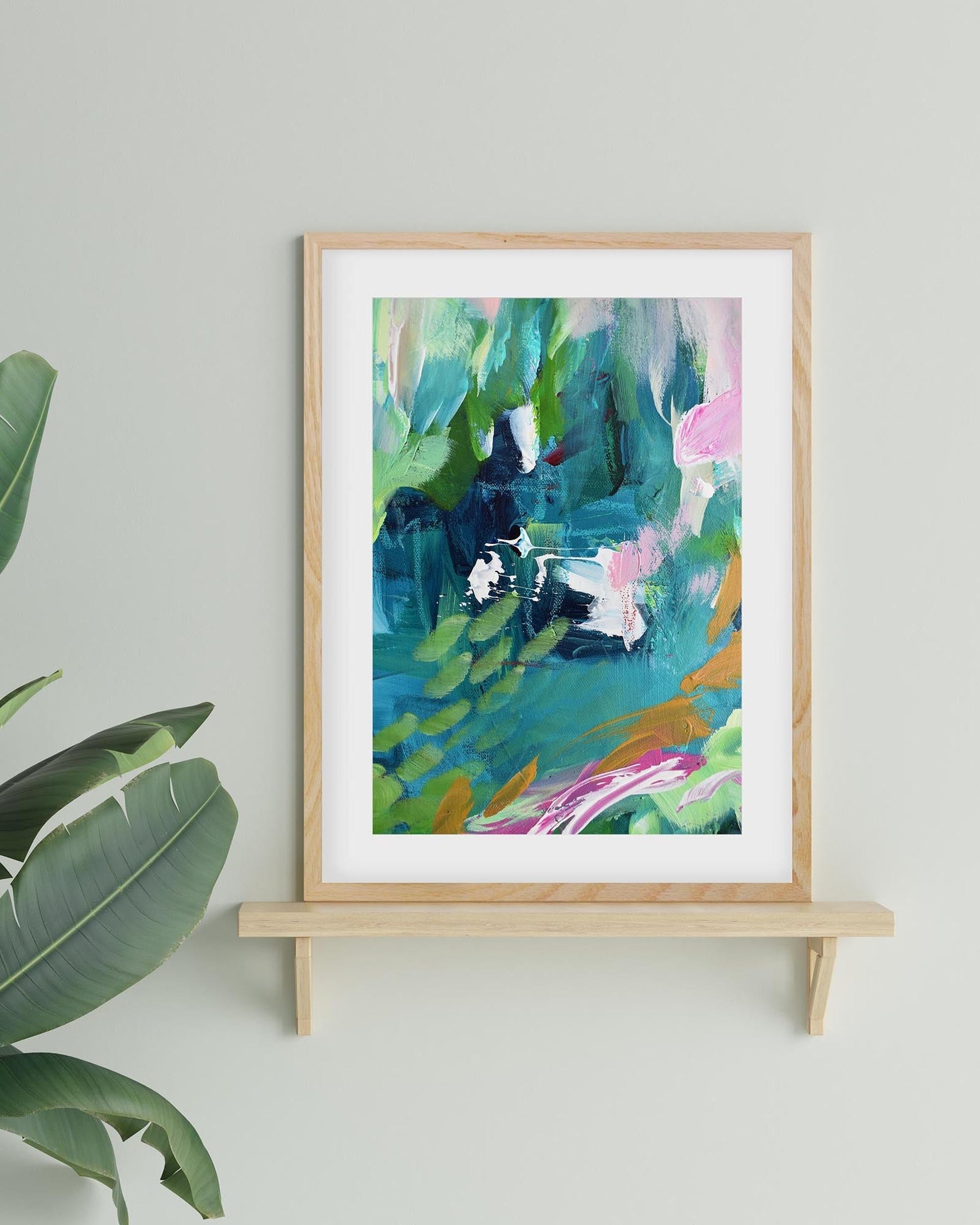 Framed abstract art print on a wooden shelf with a plant in the corner.