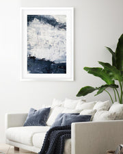 Framed abstract art above a white sofa with blue and gray pillows in a living room.