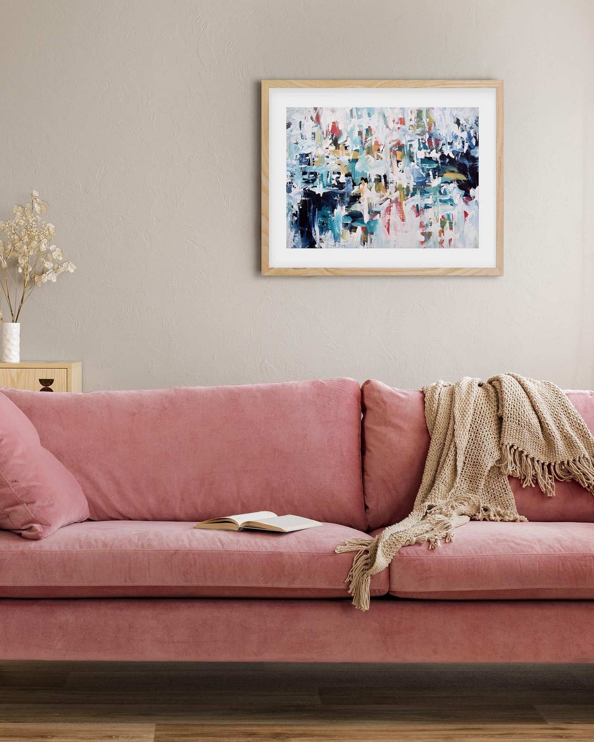 Pink sofa in a living room with a colorful abstract painting on the wall.