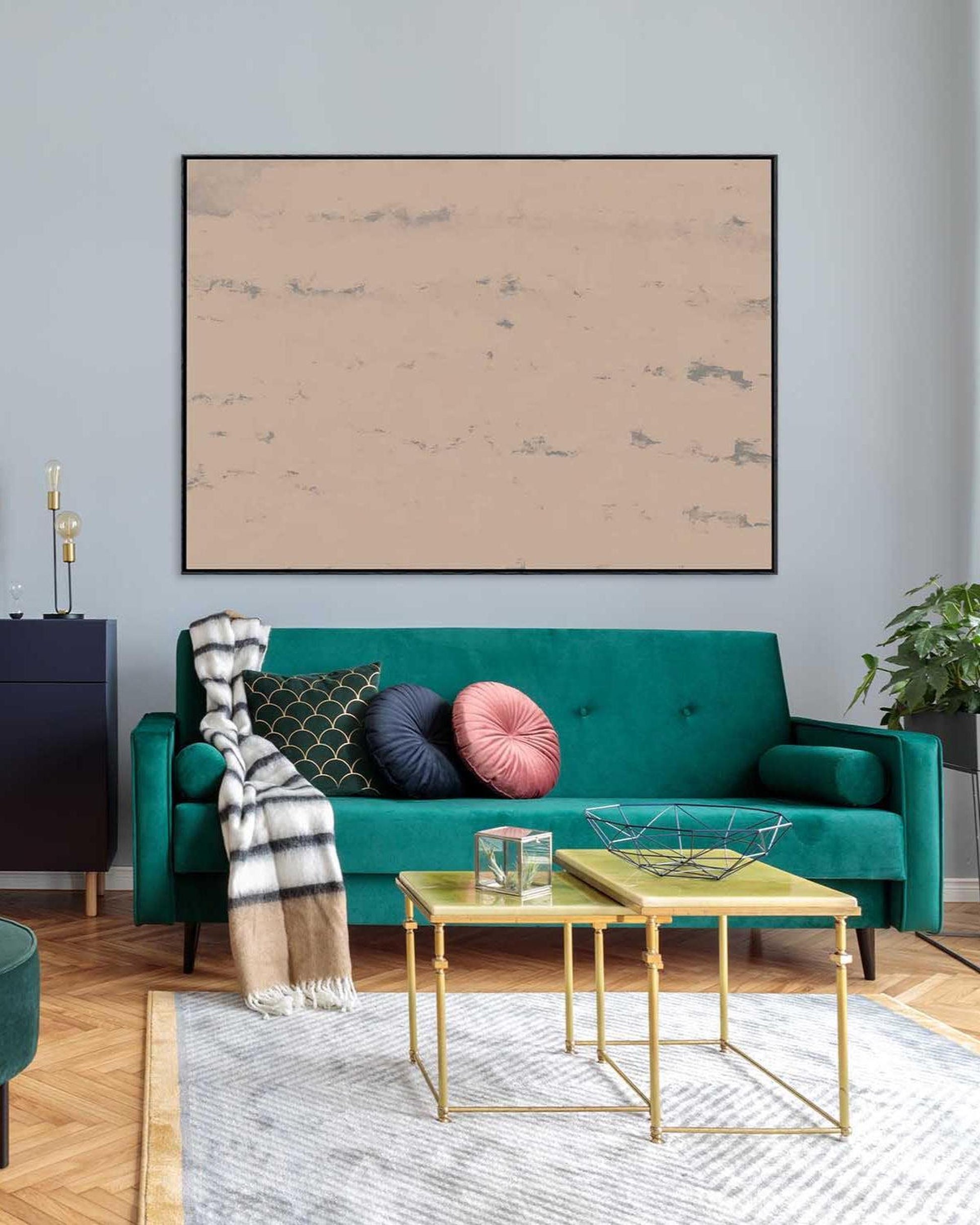 Modern living room with a teal sofa, gold coffee table, and abstract art on the wall.