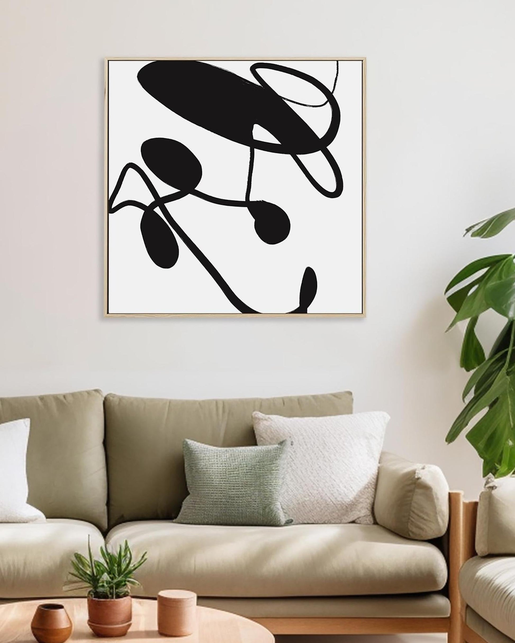 Abstract black and white artwork on a wall above a beige sofa with decorative pillows.