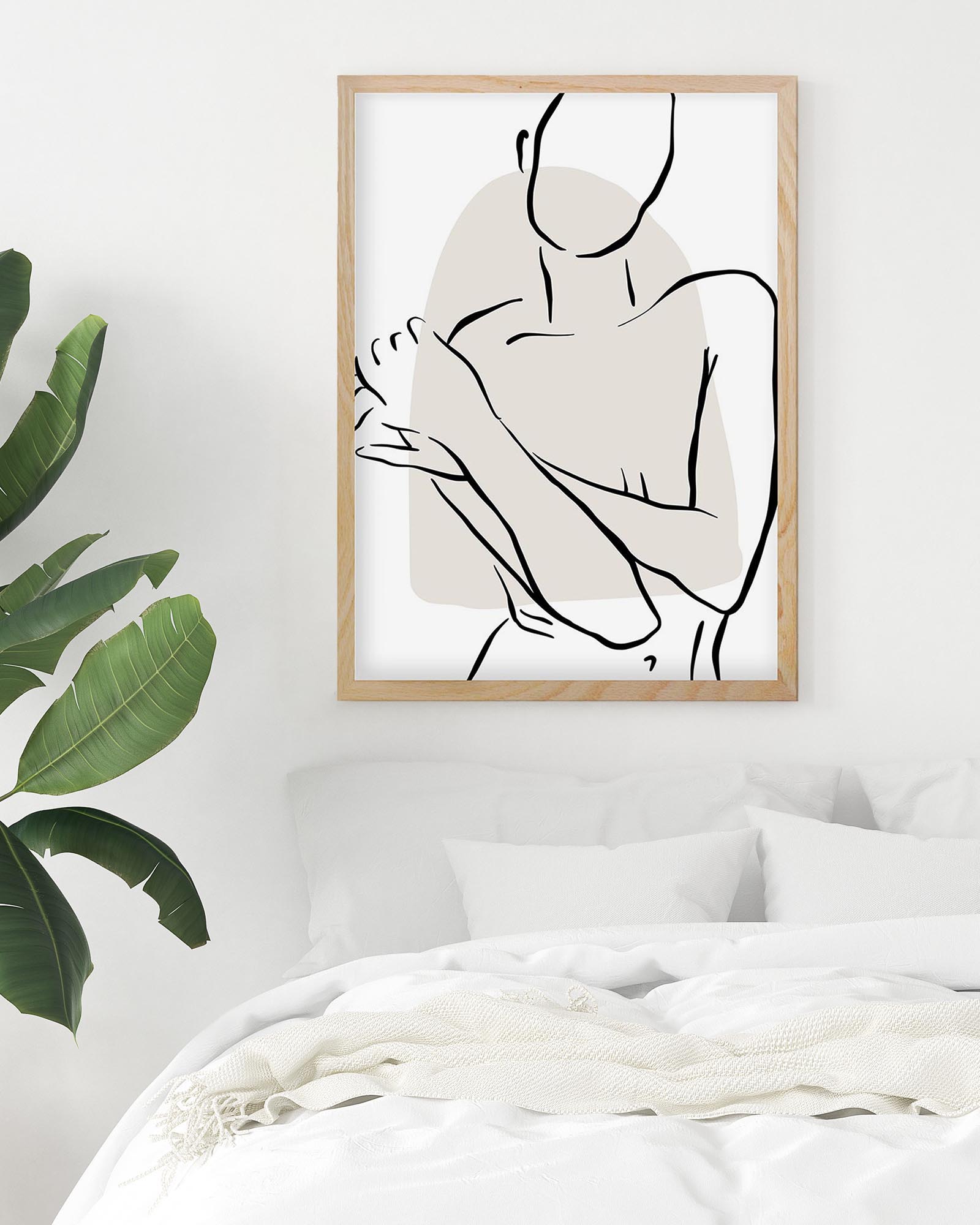 Framed abstract art print of a person on a white wall above a bed with a plant to the left.