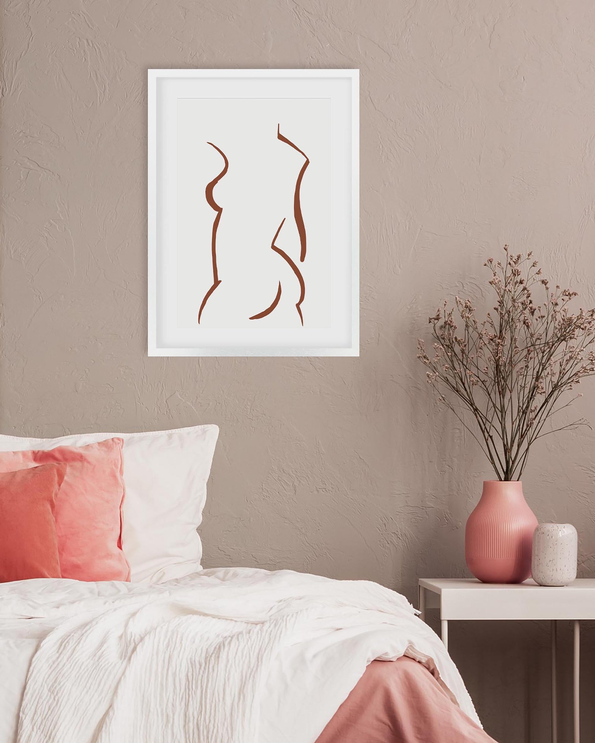 Framed abstract art above a bed with pink and white pillows and a vase on a nightstand.