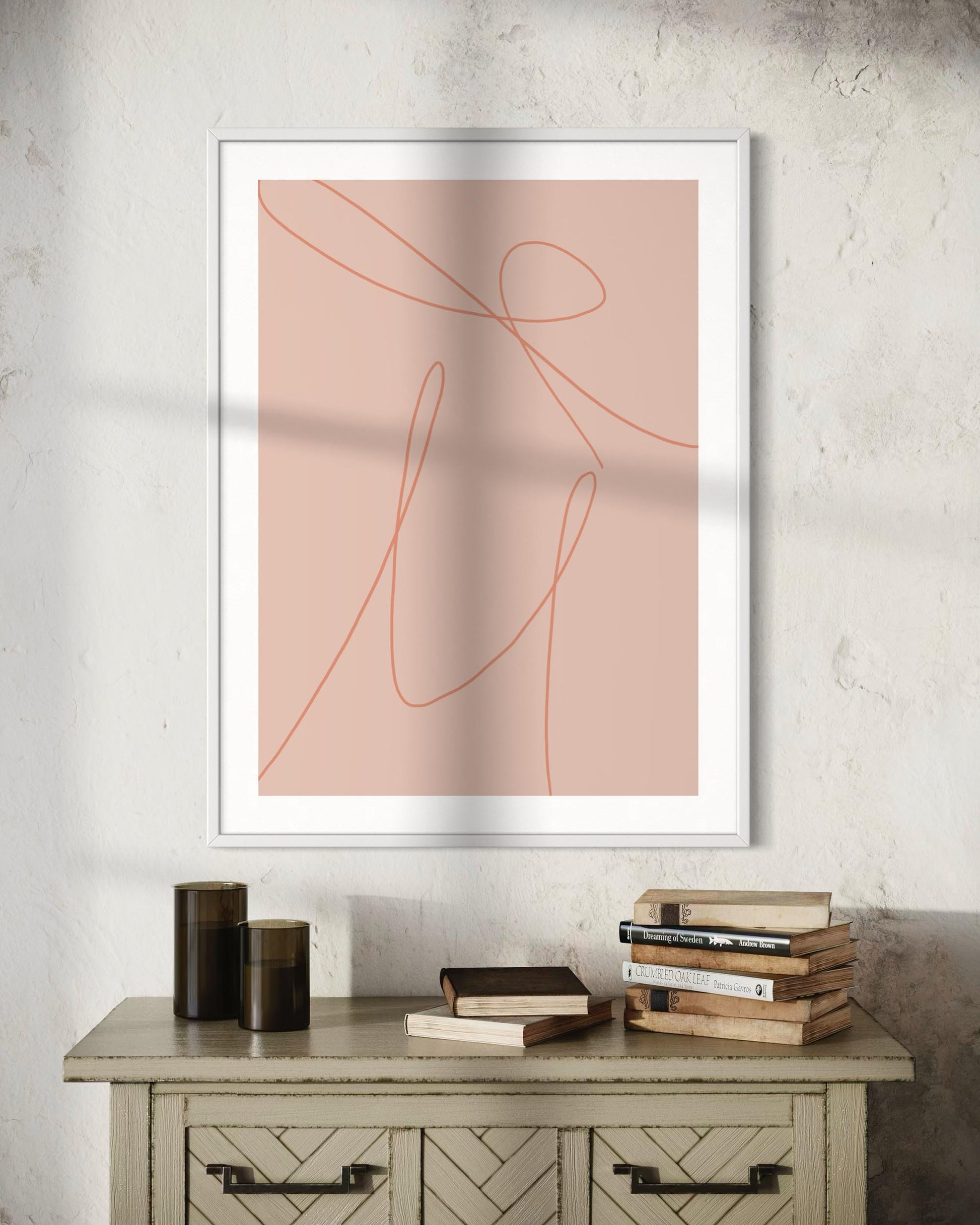 Framed abstract art print on a wall above a wooden cabinet with books.