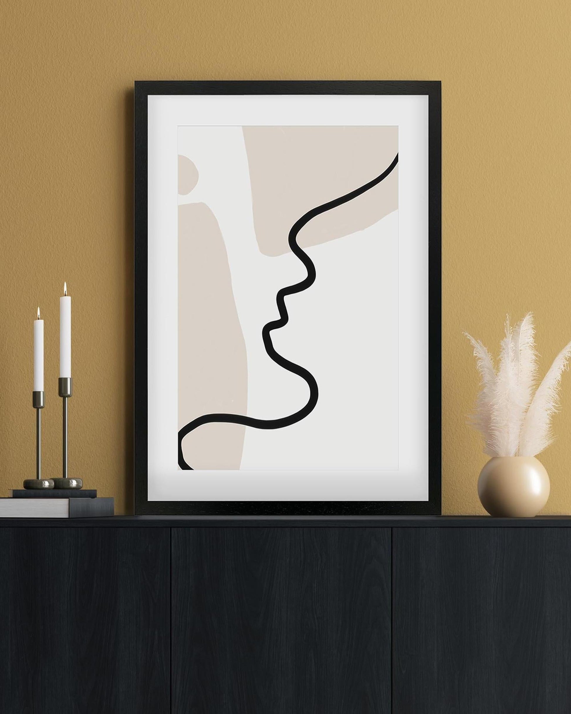 Framed abstract art print of two faces on a wall with candles and decor.