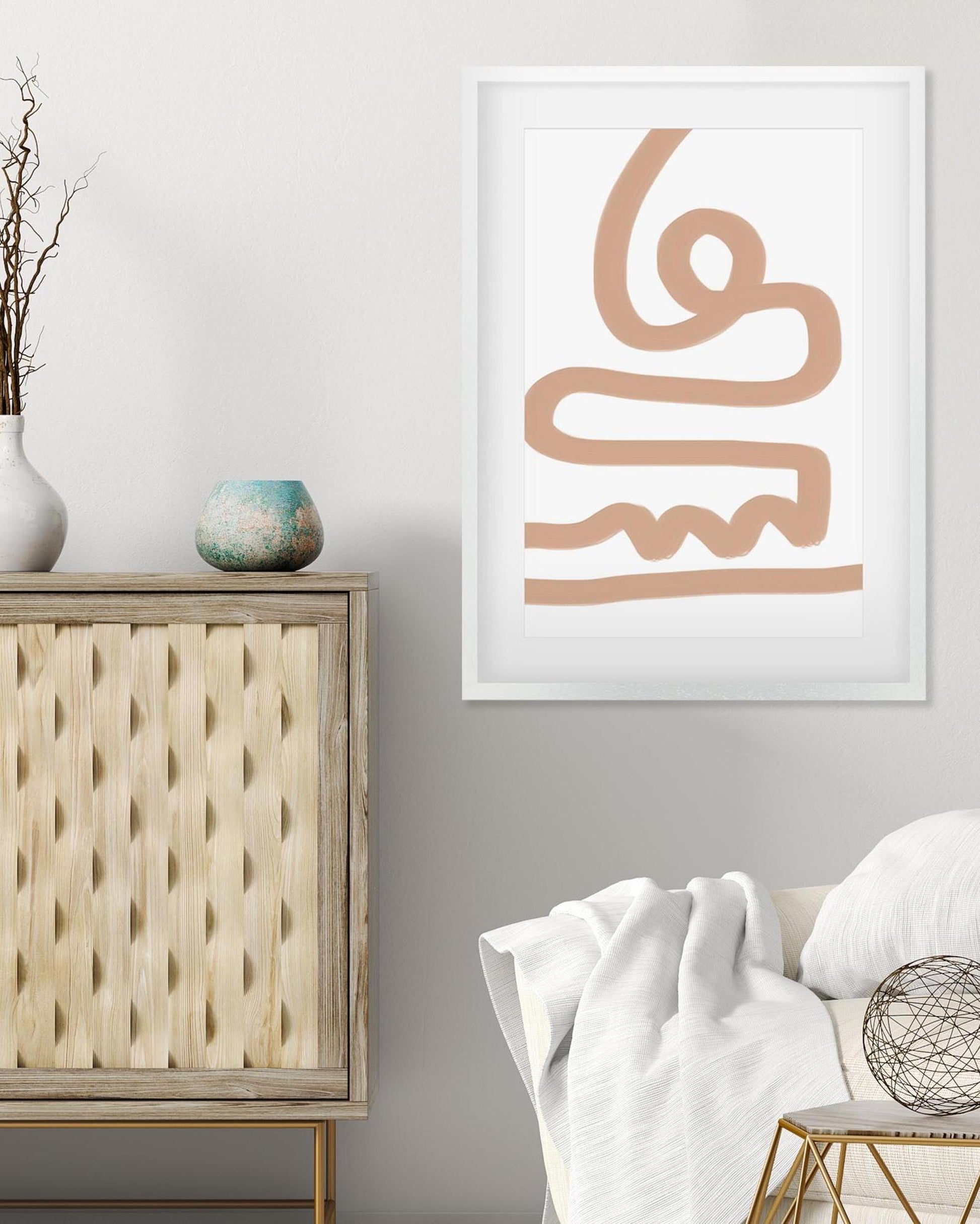 Framed abstract art piece on a wall above a wooden cabinet and chair.