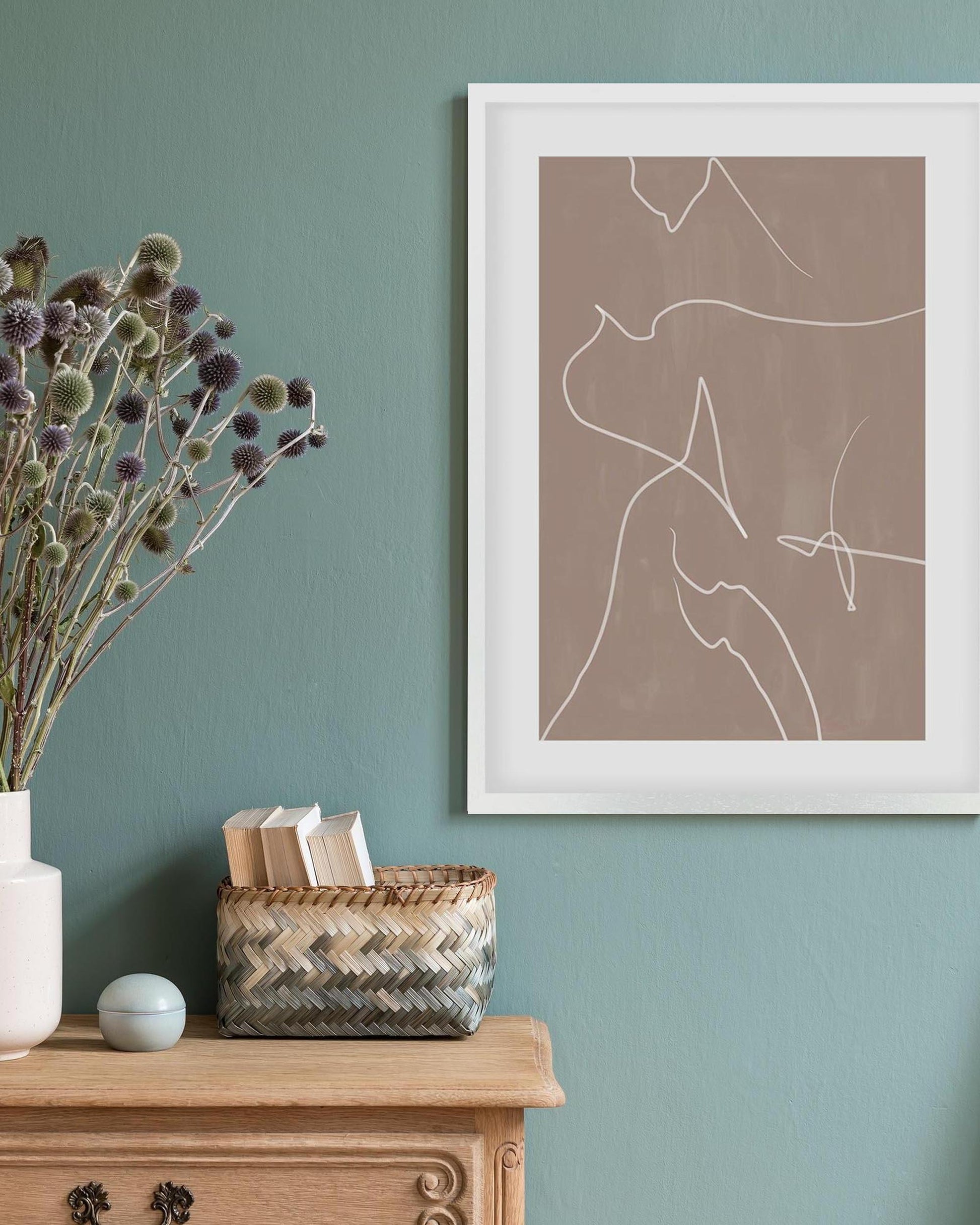 Framed abstract art on a teal wall with a wooden cabinet and decorative items.