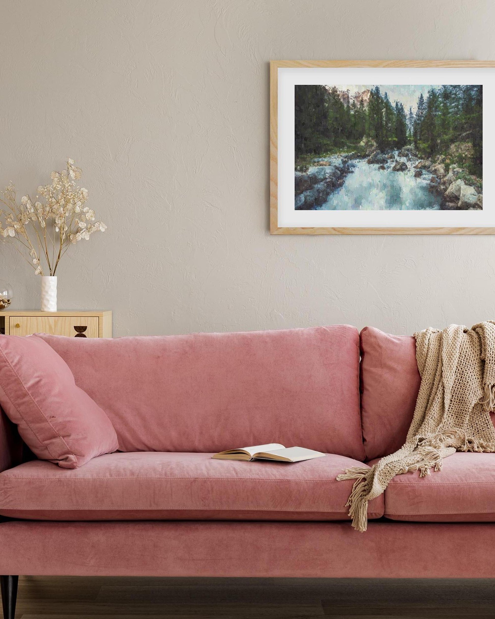 Pink sofa in a living room with a framed picture of a forest on the wall.