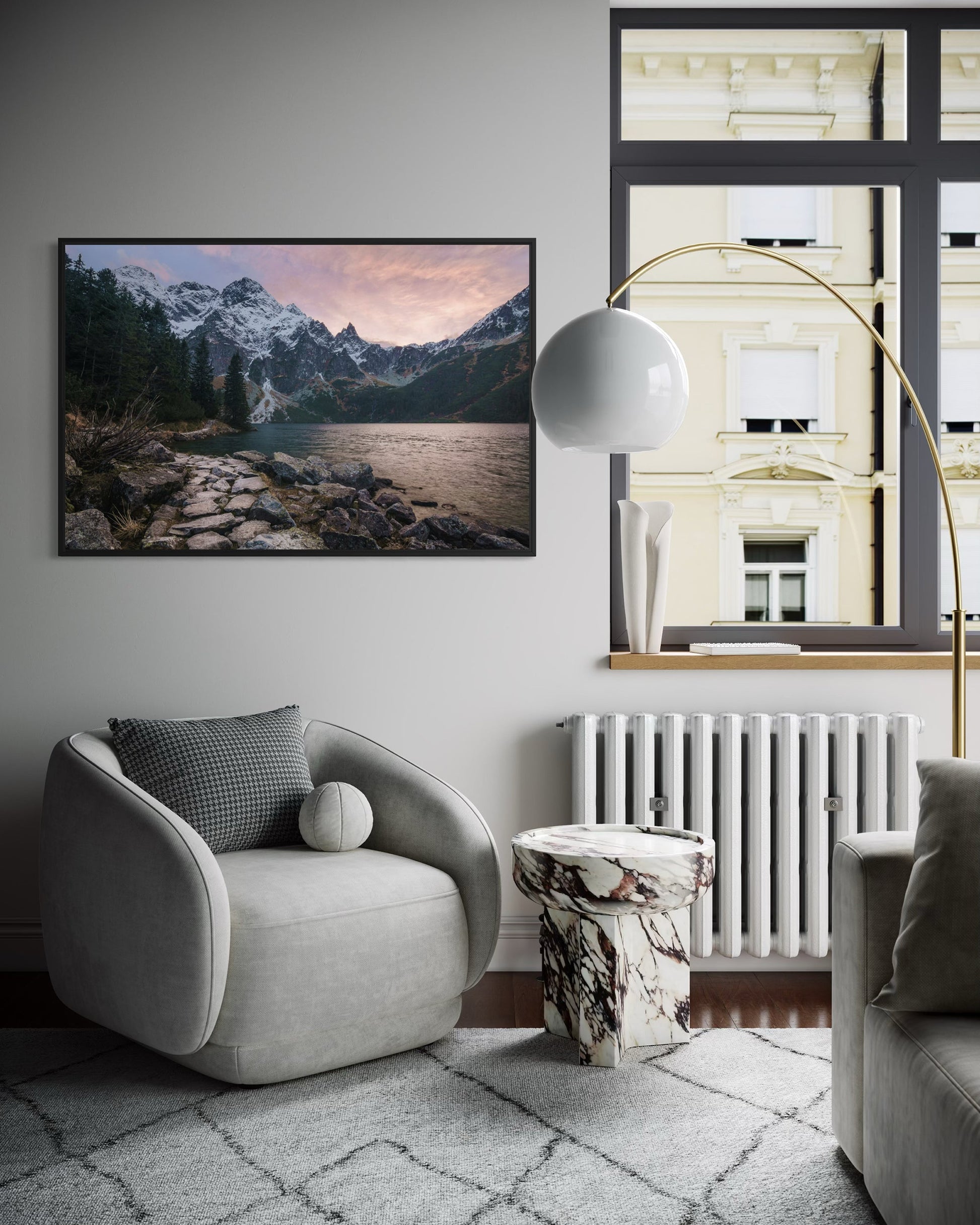 Modern living room with a gray armchair, marble side table, and mountain landscape artwork.