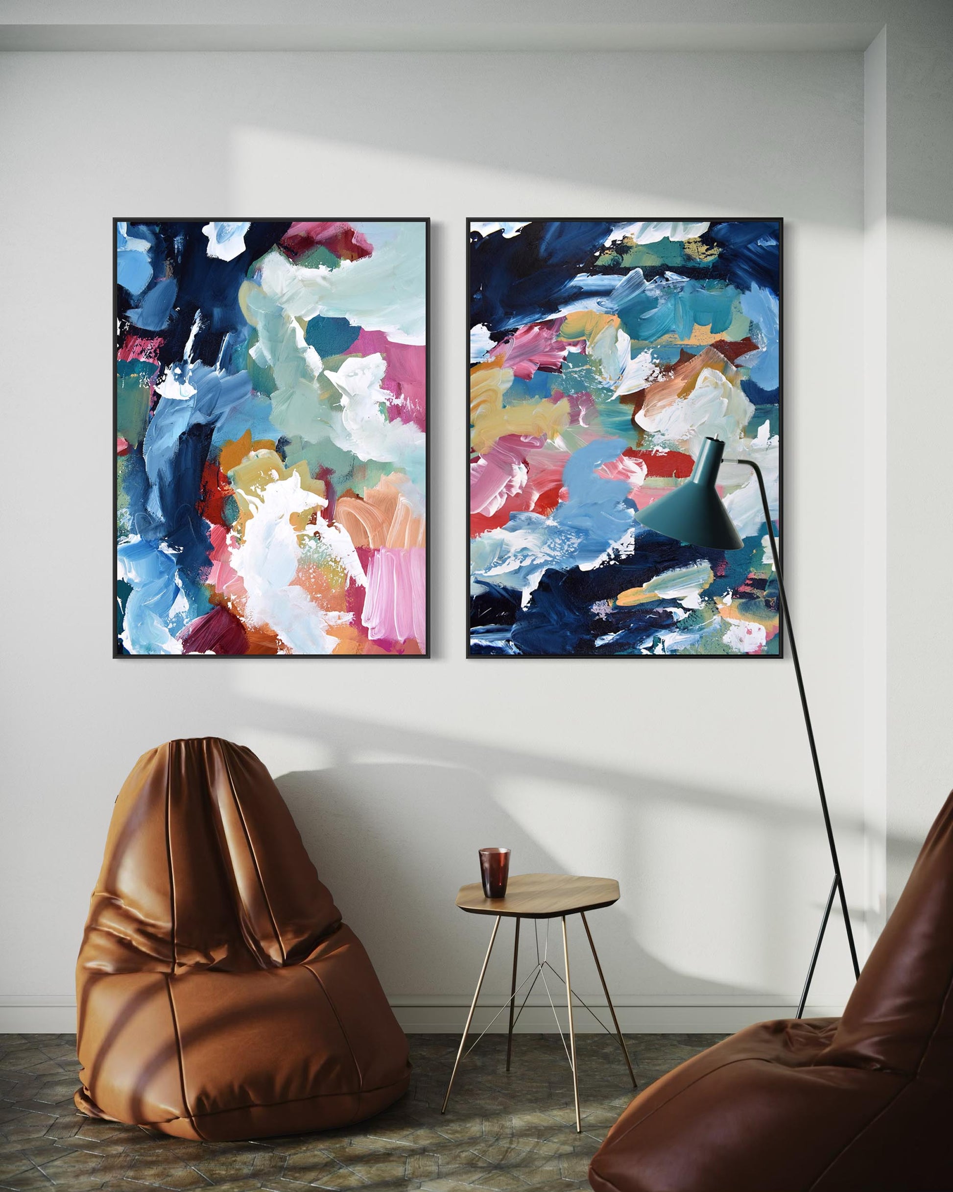Two abstract paintings on a wall with a brown bean bag chair and small table below.