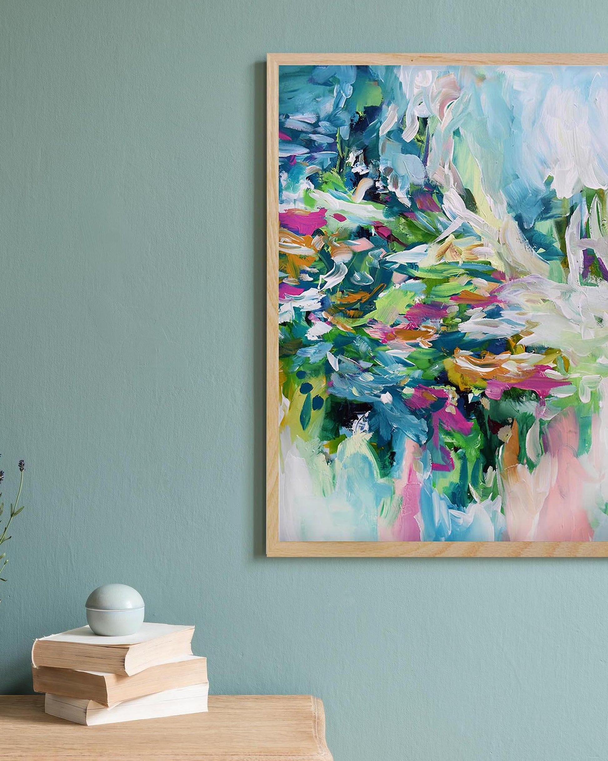 Colorful abstract painting on a light blue wall with books and a small plant.