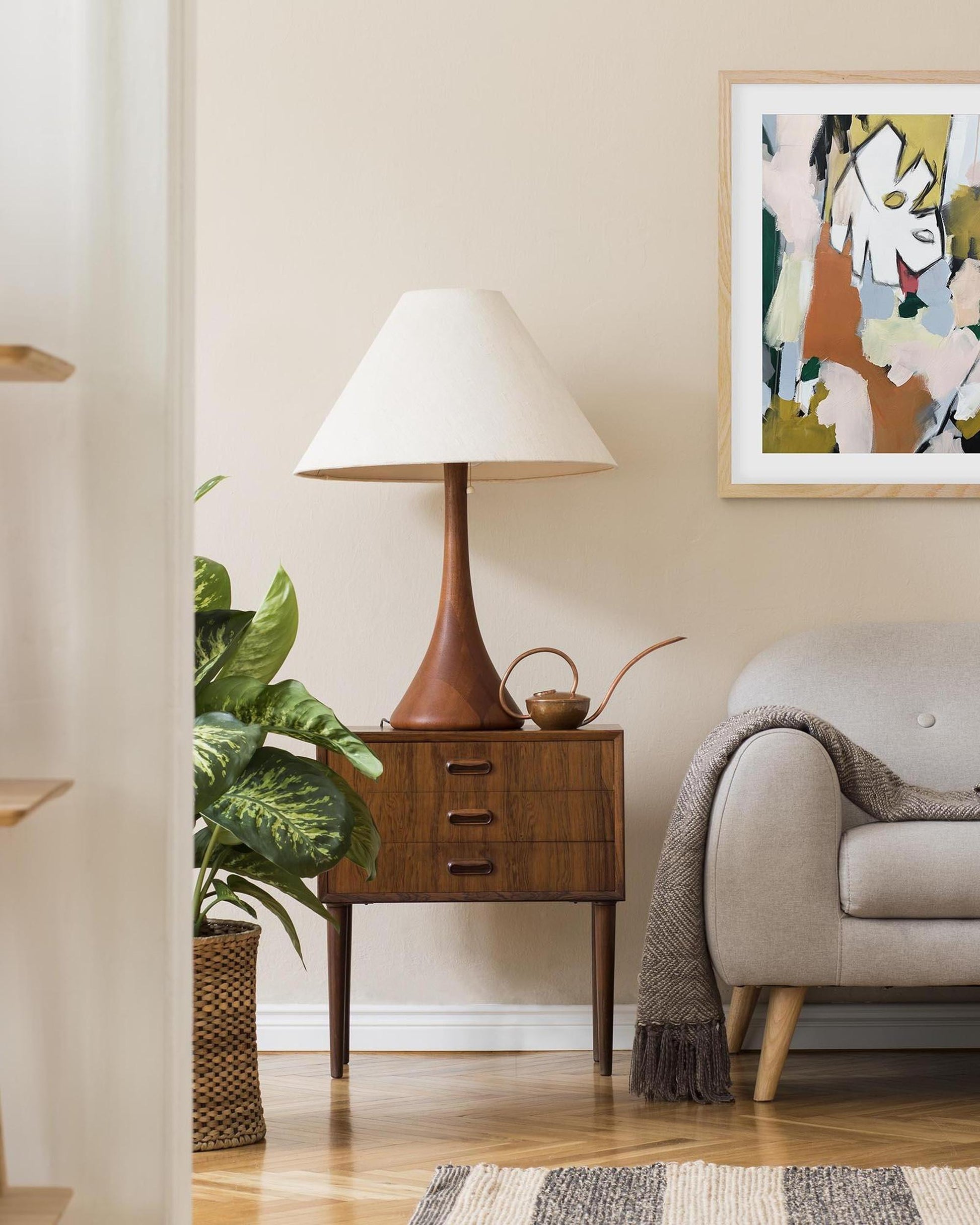 Nursery room with wooden nightstand, lamp, and sofa.