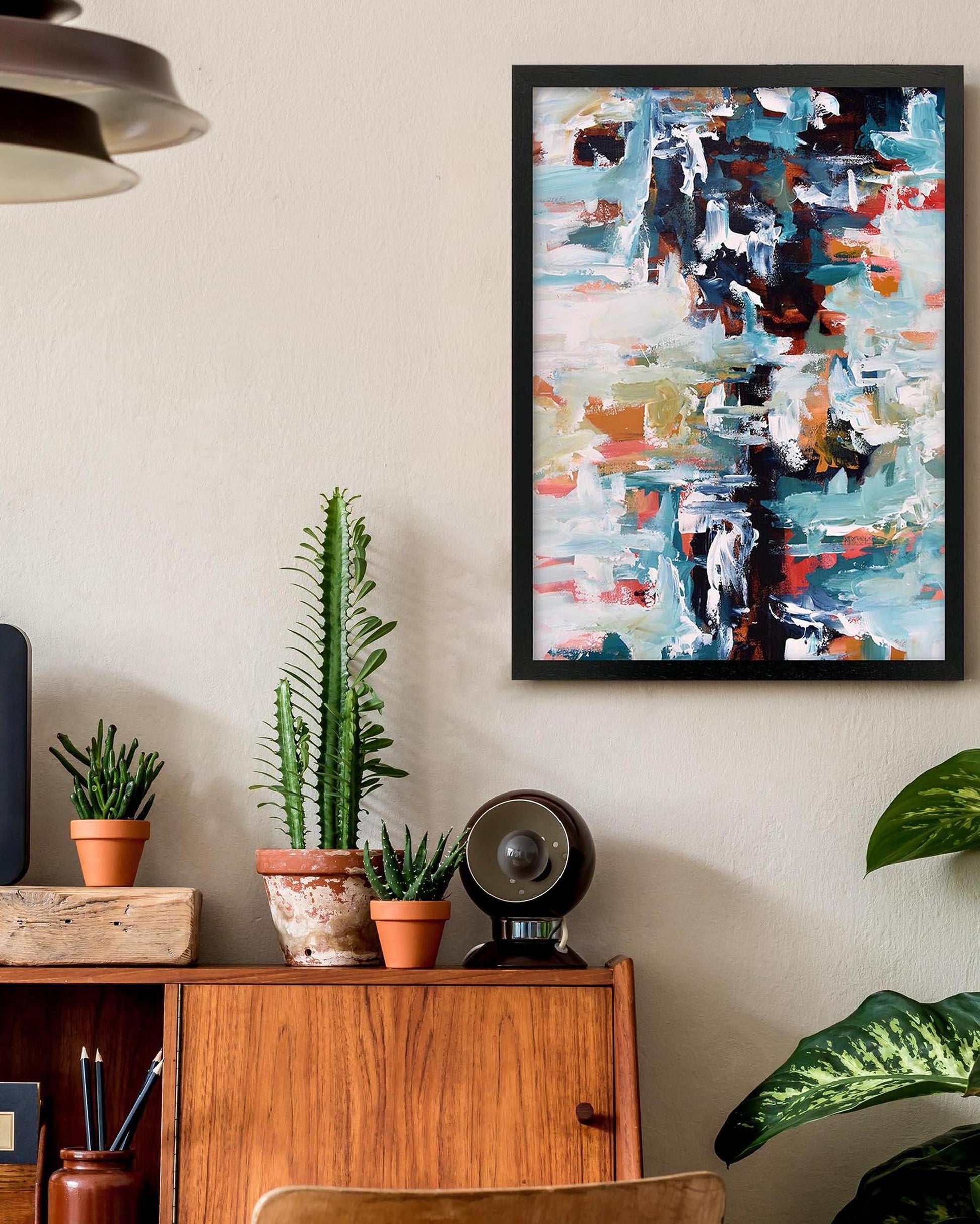 Abstract painting on a wall above a wooden cabinet with plants