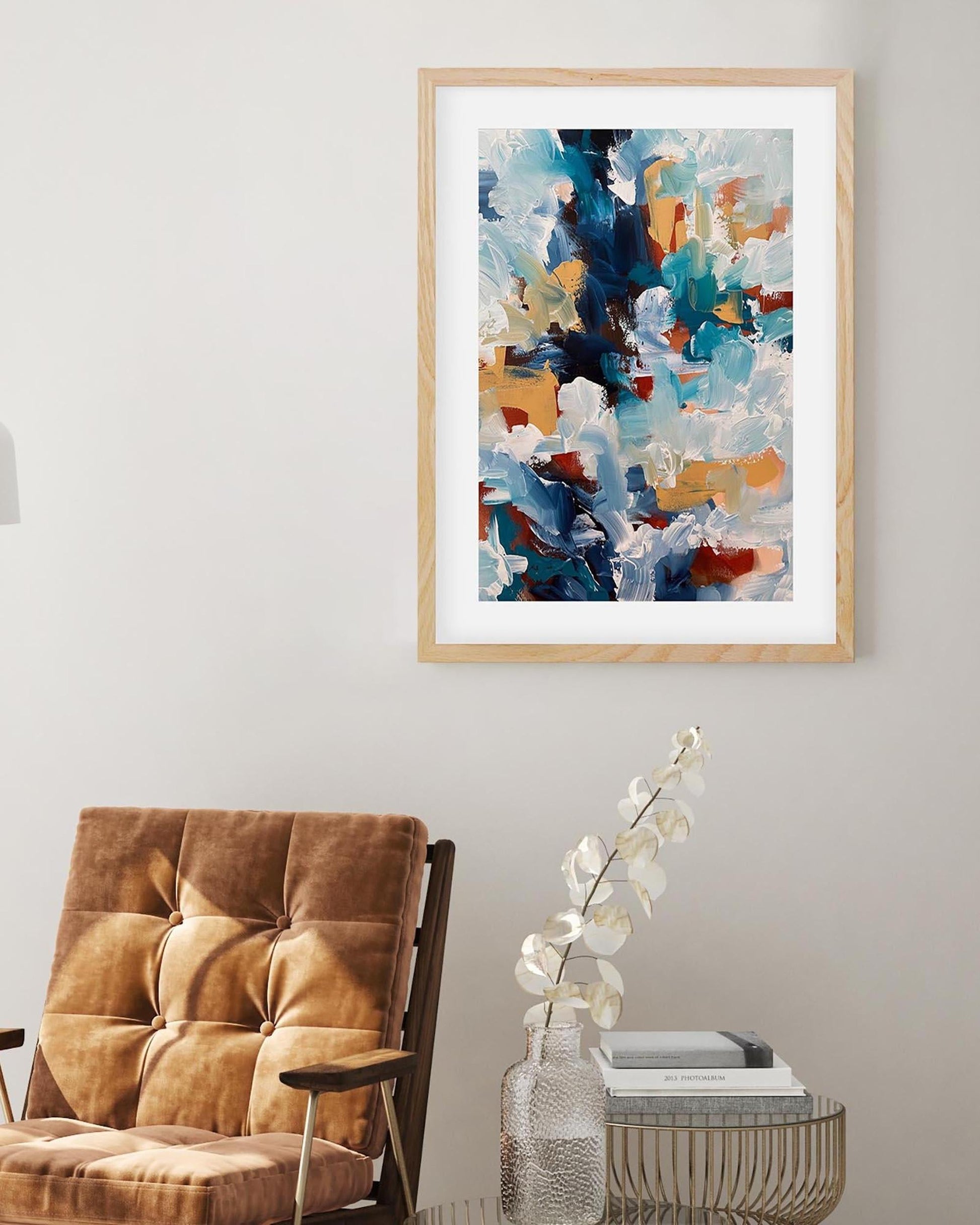 Abstract art print in a wooden frame on a wall above a brown armchair.