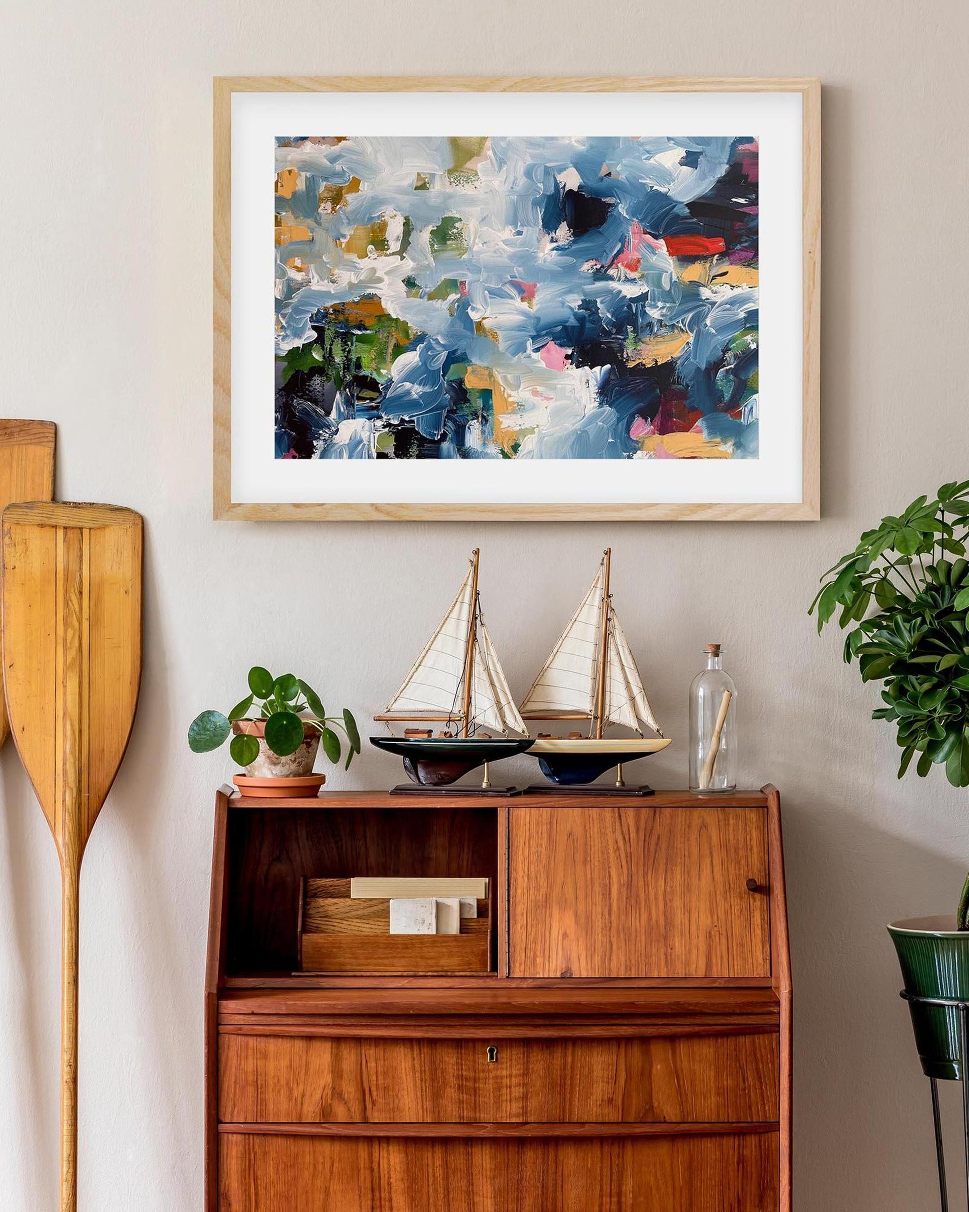 Framed abstract art above a wooden cabinet with decorative items