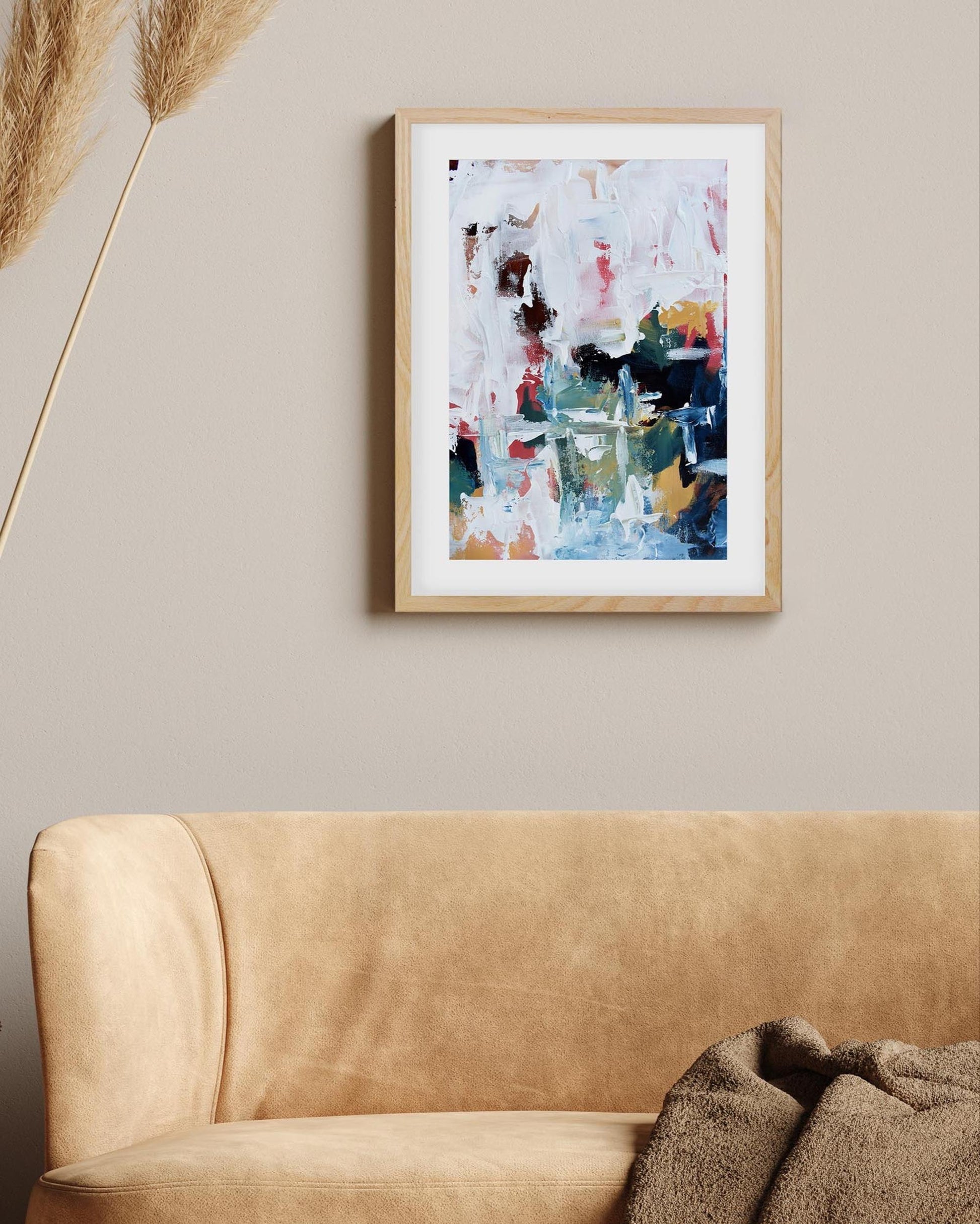 Abstract art print in a wooden frame on a beige wall above a beige sofa.