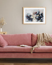 Pink sofa with a blanket and a framed abstract painting on a beige wall.