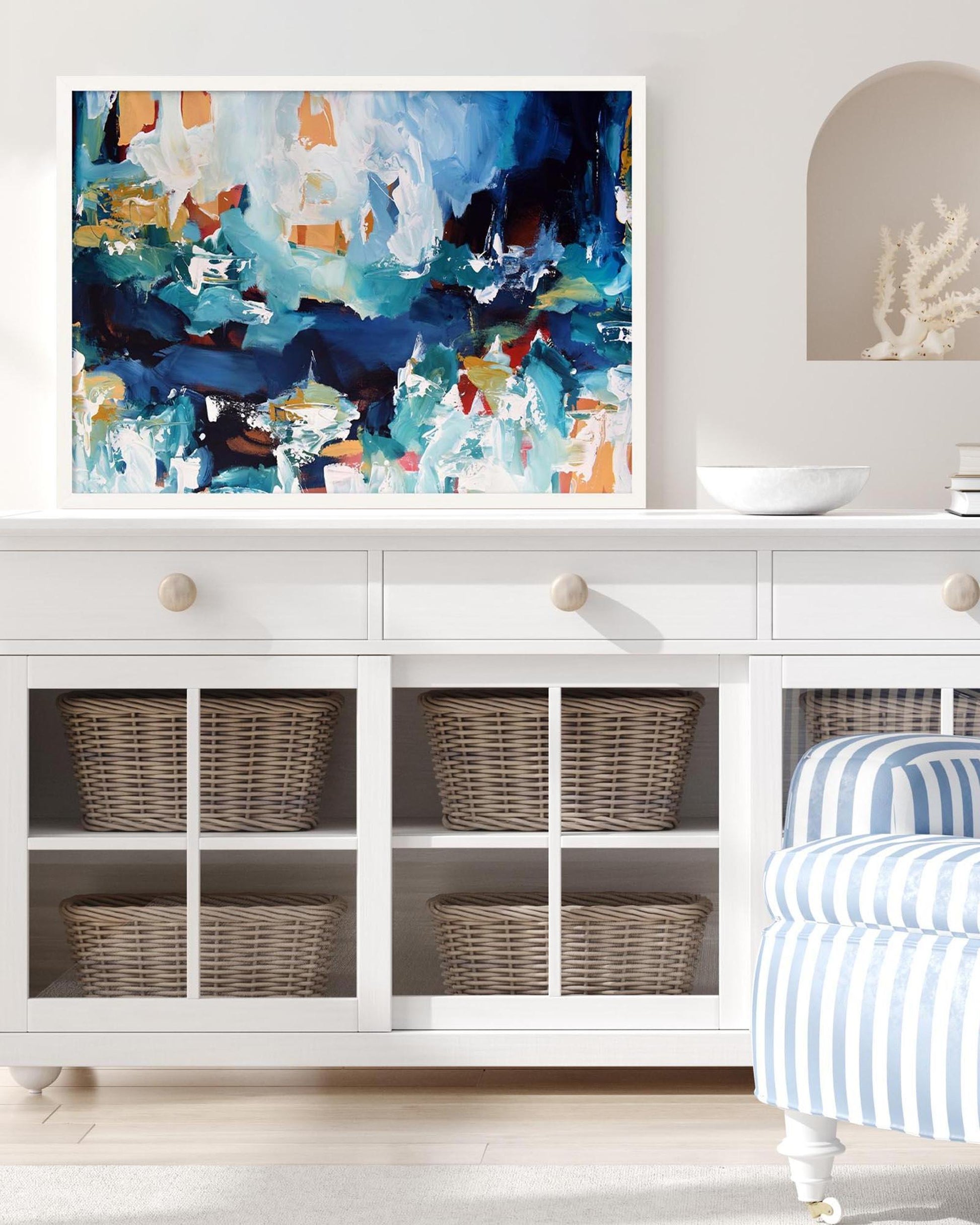Abstract painting on a white wall above a white cabinet with wicker baskets.