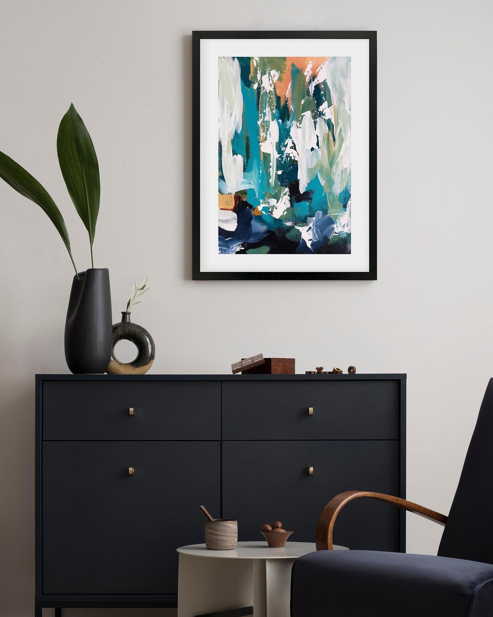 Framed abstract art piece on a wall above a black dresser with decorative items.
