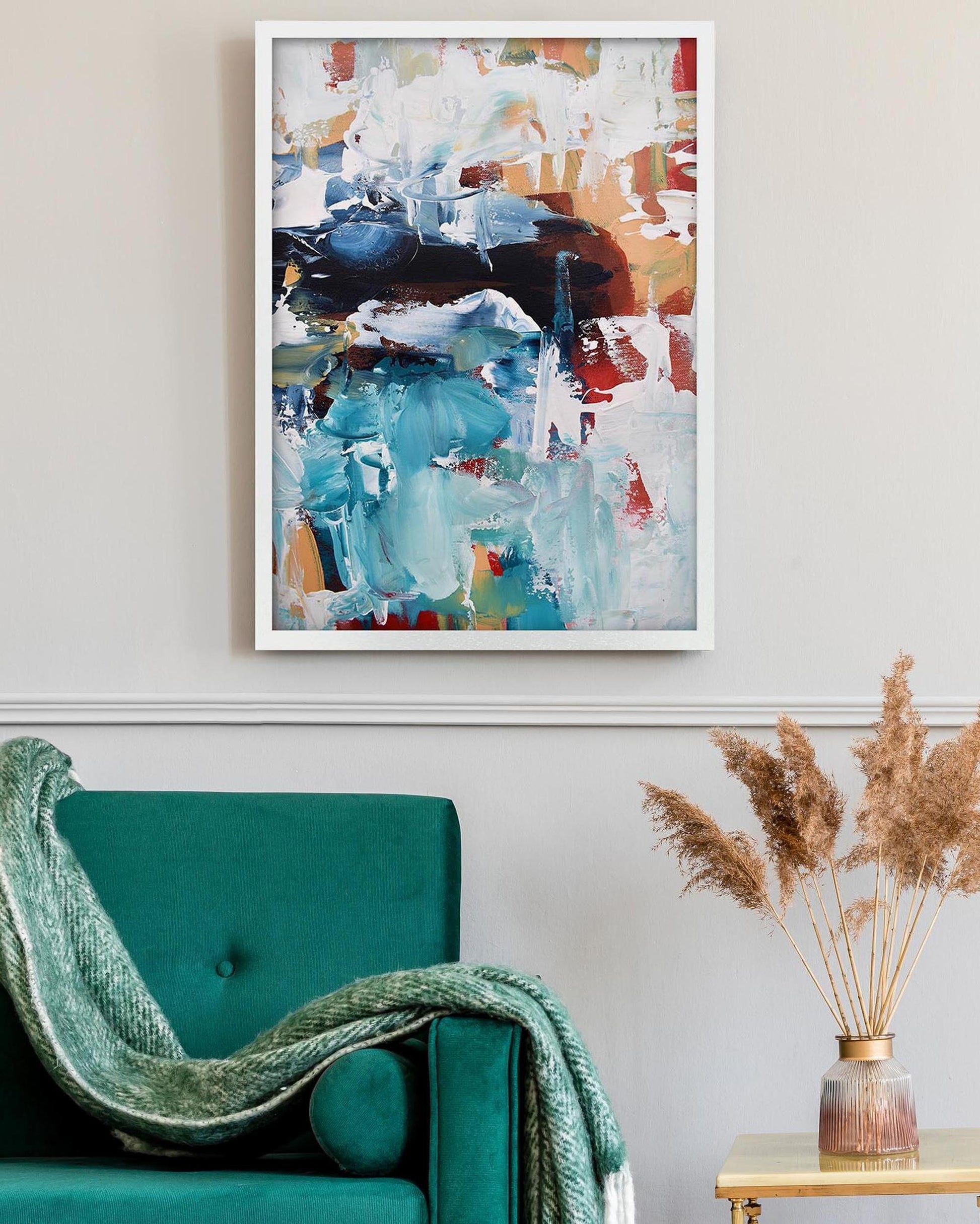 Abstract art print on a wall above a teal sofa with a vase of dried plants on a table.