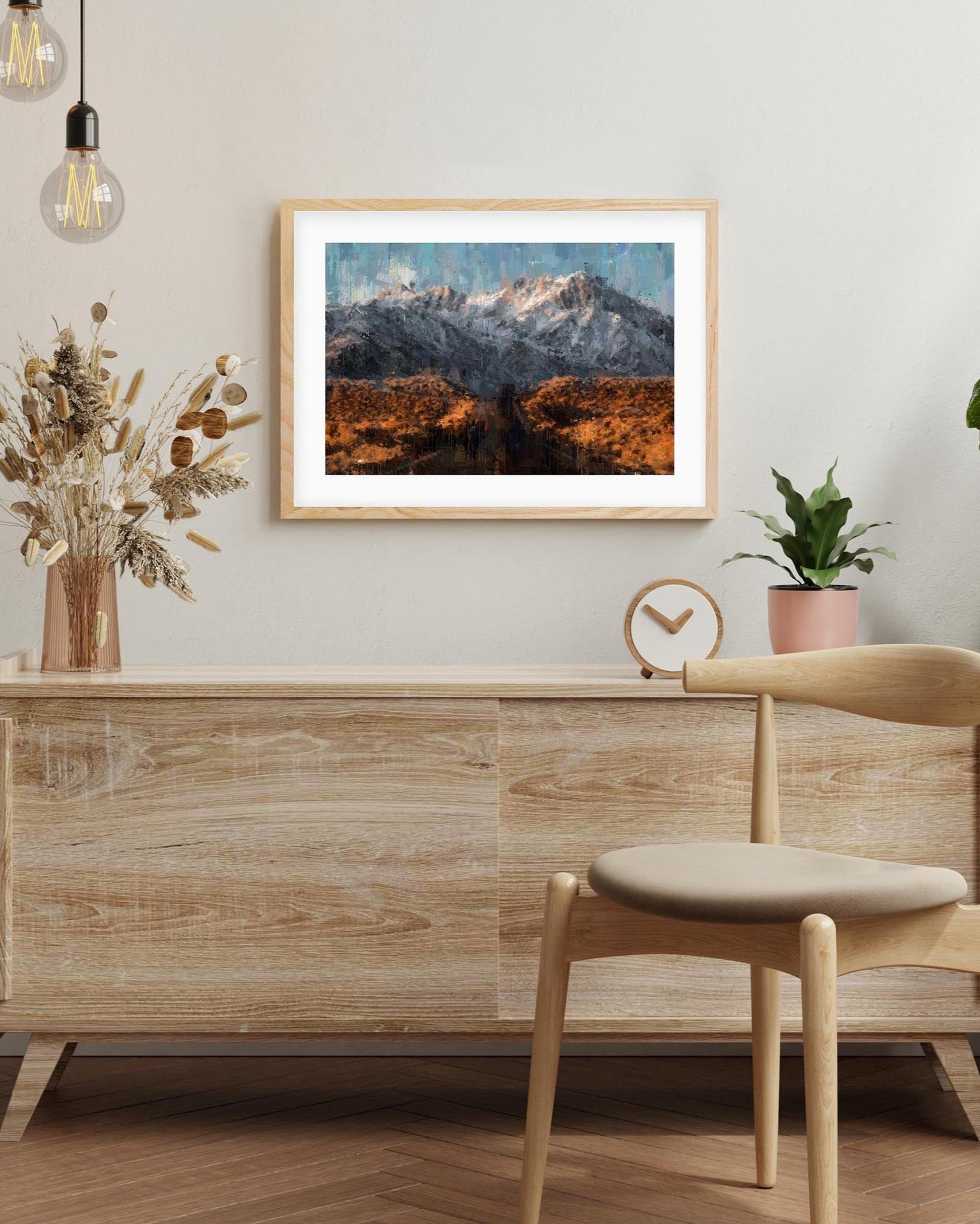 Wooden desk with chair, framed mountain landscape art, and decorative elements in a room.