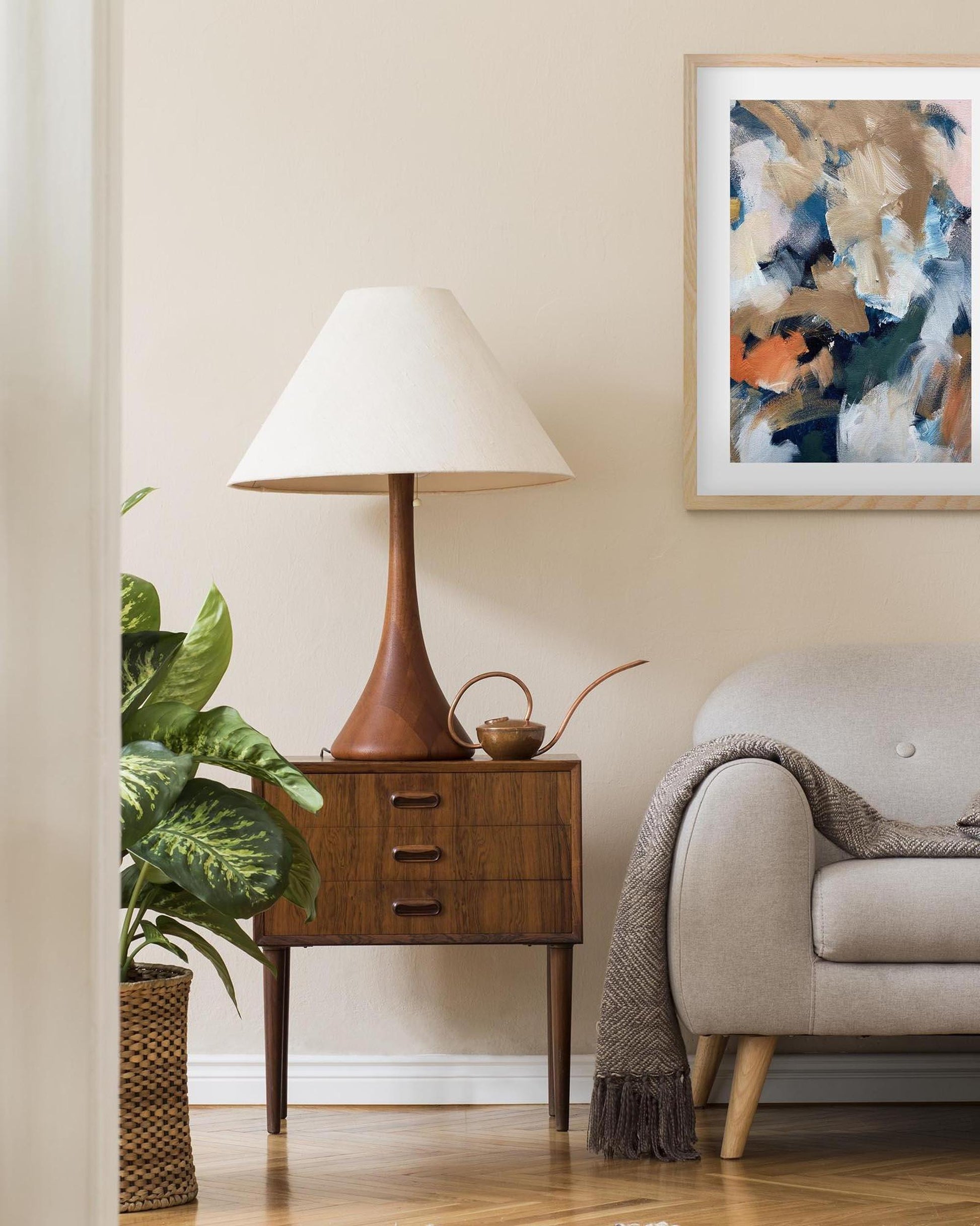 Living room with a lamp on a side table, plant, and abstract art on the wall.