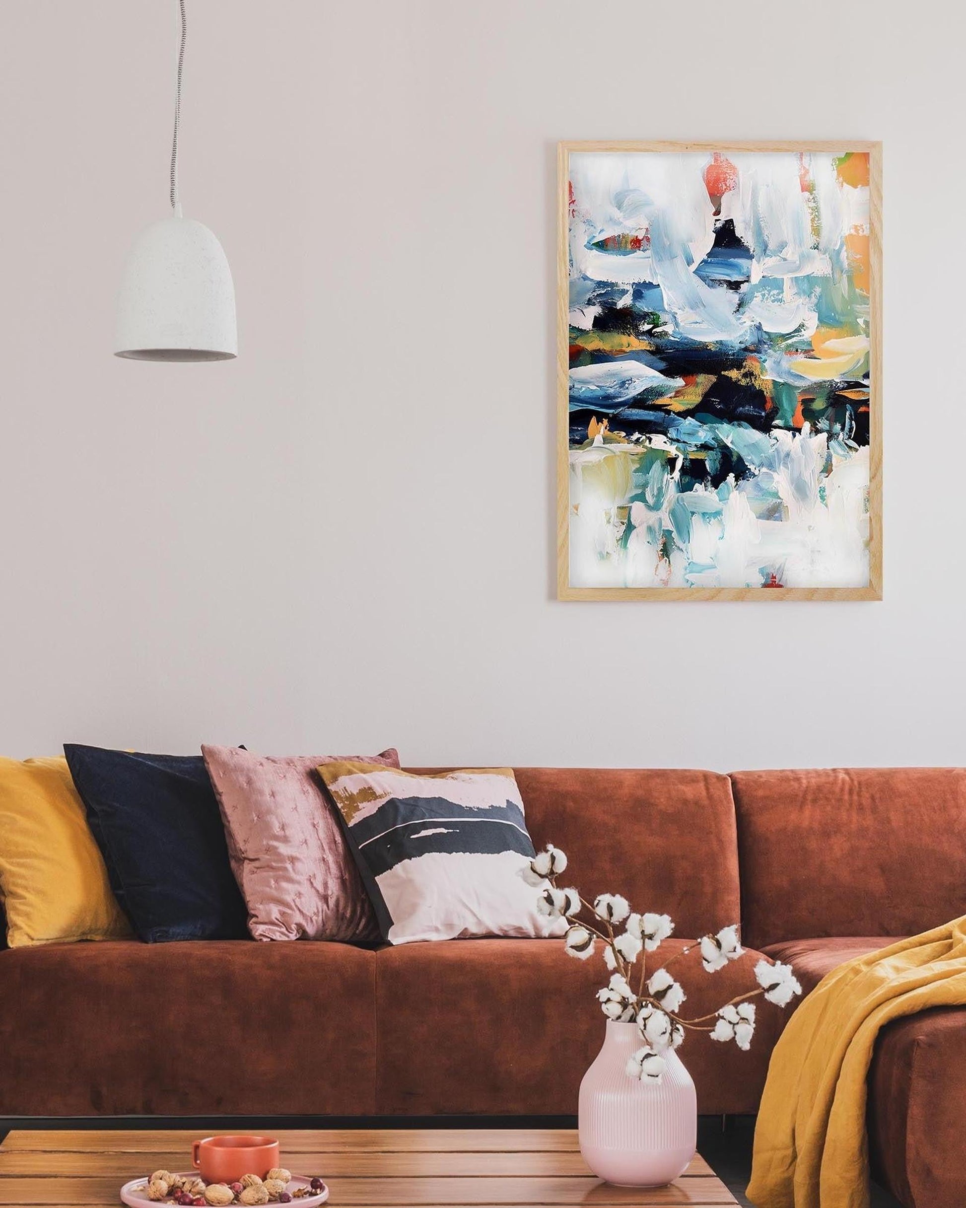 Living room with a brown sofa, colorful pillows, a wooden coffee table, and a framed abstract painting on the wall.