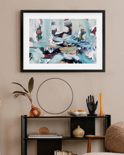 Framed abstract art piece on a wall above a shelf with decorative items.