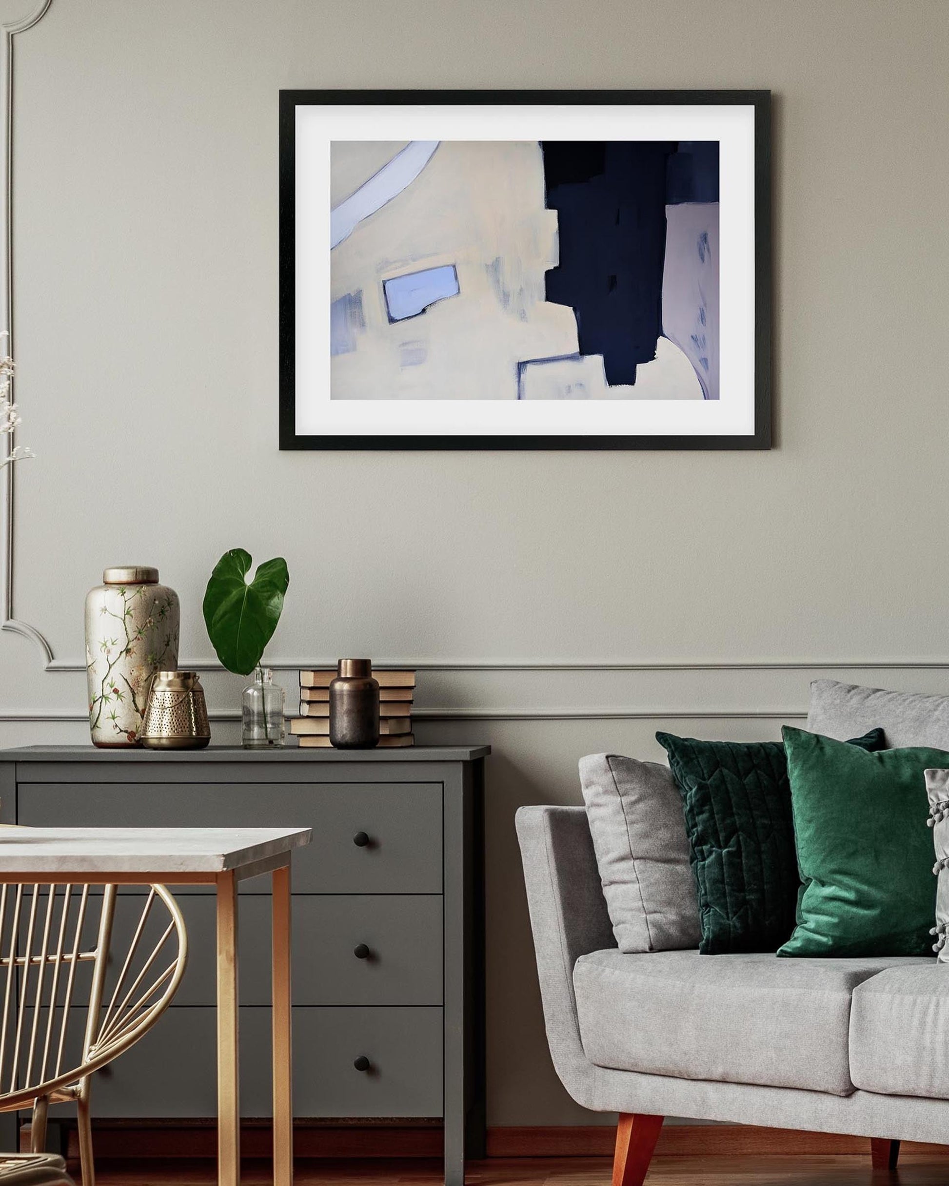 Living room with a framed abstract painting on the wall, a gray sofa with green and gray pillows, and a small table with decorative items.